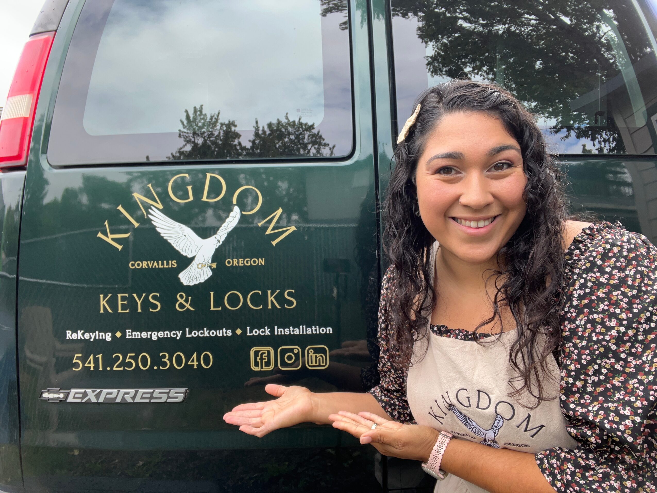 Woman smiling and pointing at a vehicle with Kingdon Keys & Locks logo, contact info, and social media icons.