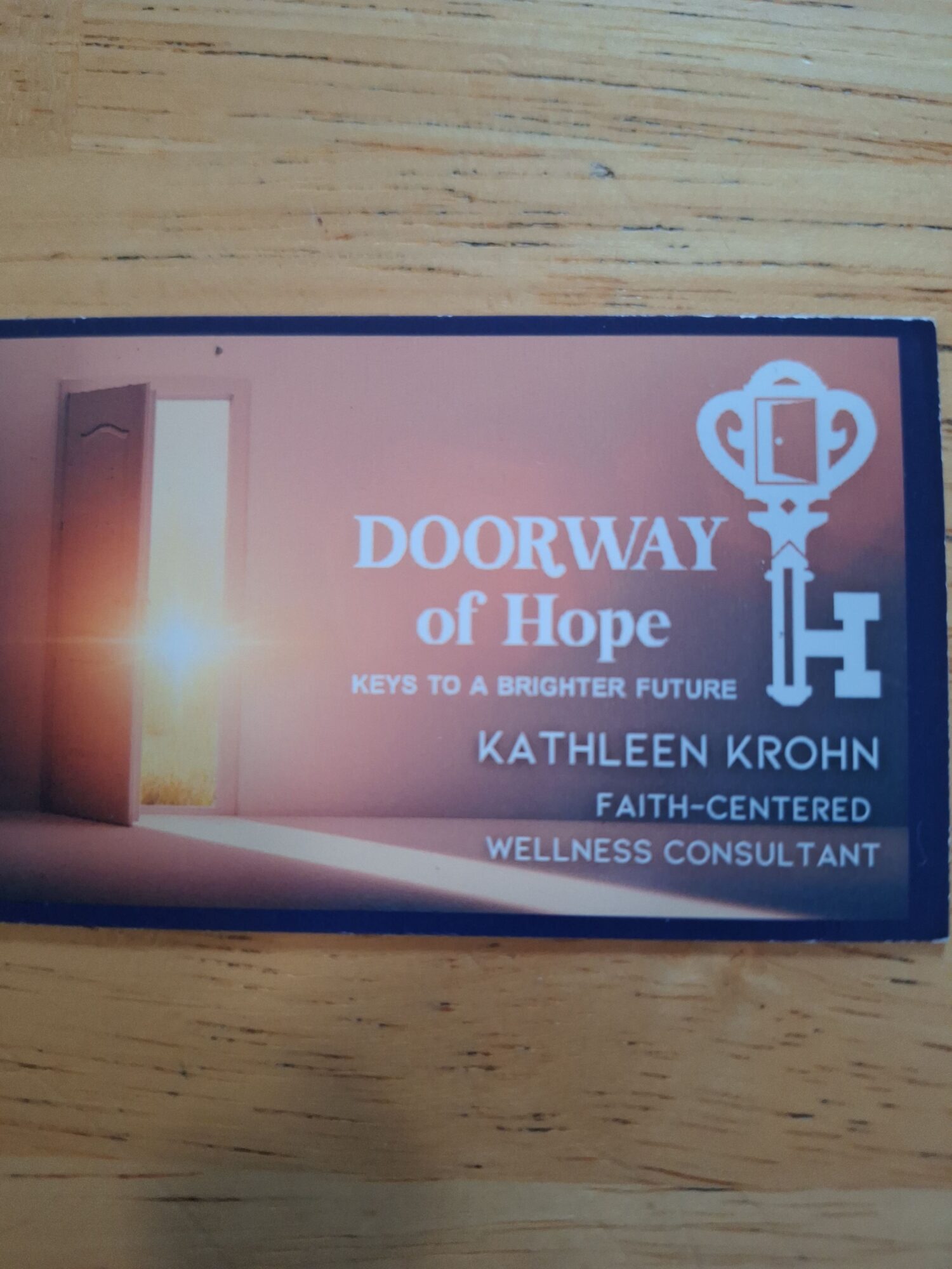 Business card with text and logo on a wooden surface, oriented sideways.