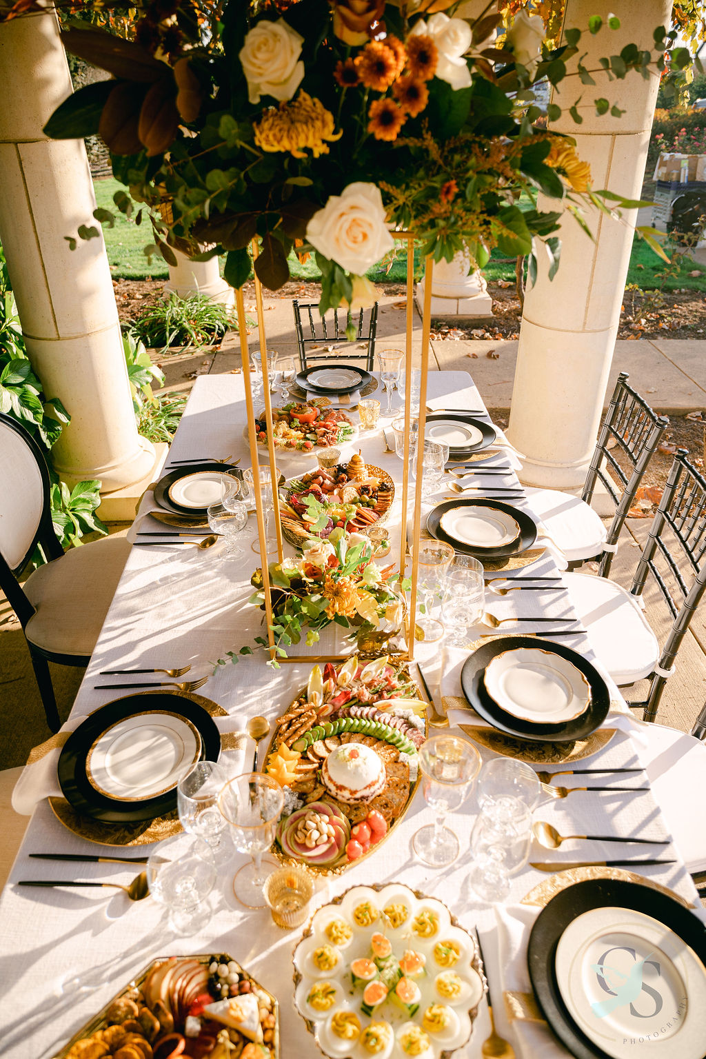 Elegant table setting with a floral centerpiece, plates, and decorative food items, outdoors with chairs and greenery nearby.