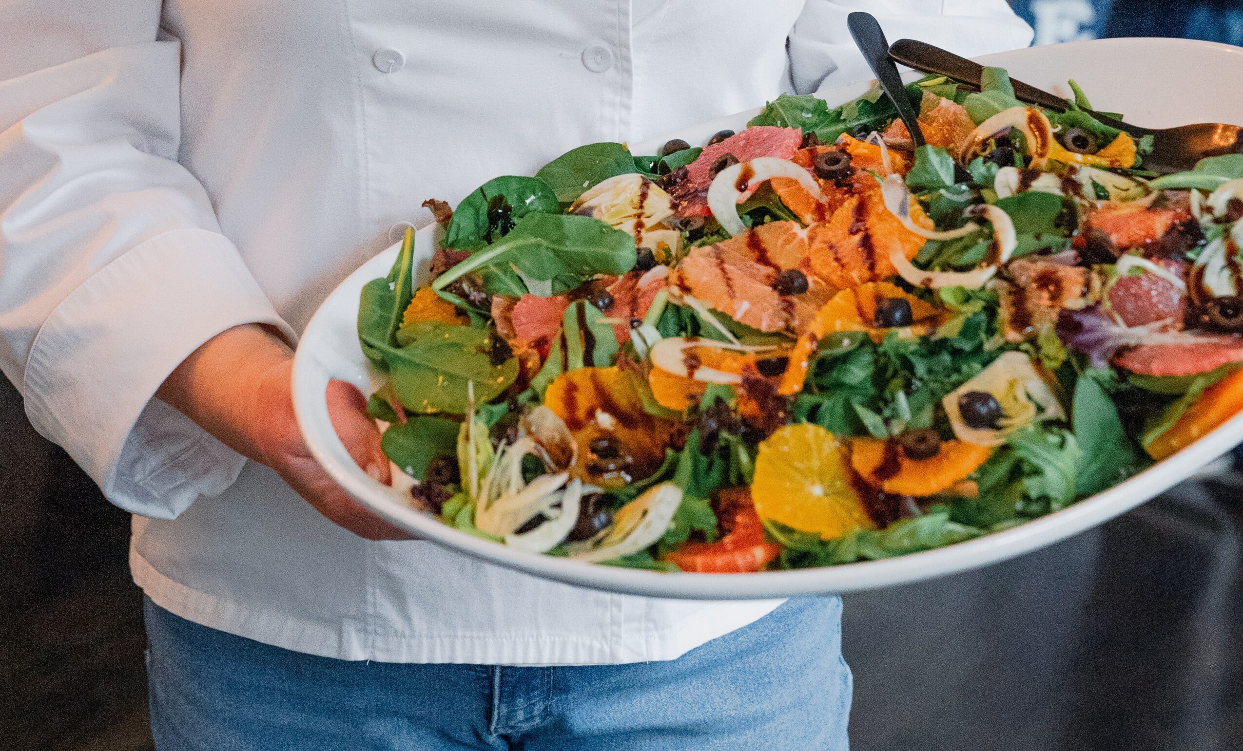 Person holding a large bowl of colorful salad with greens, vegetables, and toppings.