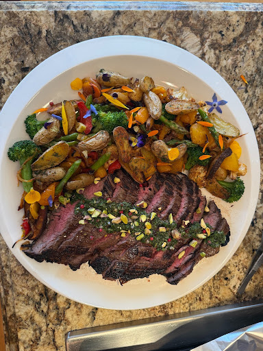 Cooked steak with grilled vegetables including broccoli, mushrooms, and bell peppers on a white plate.