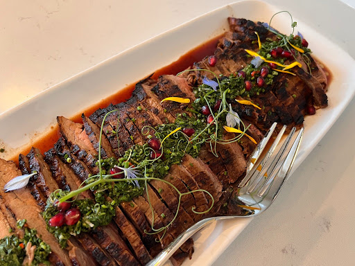 Sliced cooked meat garnished with herbs, edible flowers, and berries on a white rectangular plate.