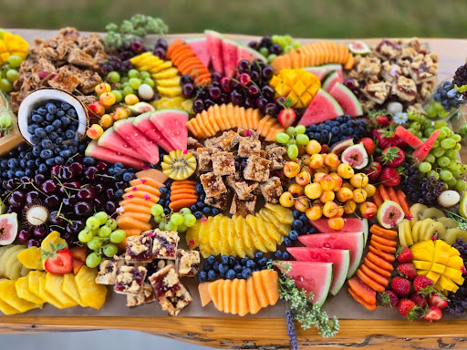 Assorted fresh fruits and snacks arranged on a tray, including watermelon, grapes, berries, and granola bars.