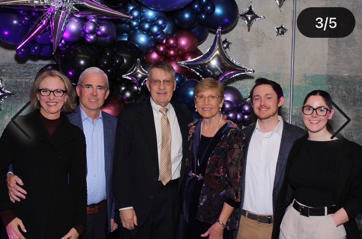 Group of six people standing together in front of colorful balloons and star-shaped decorations, smiling for the photo.