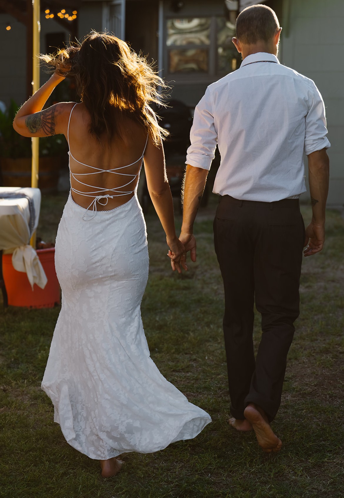 A woman in a white dress and a man in a white shirt and dark pants walk hand in hand outdoors, holding hands.