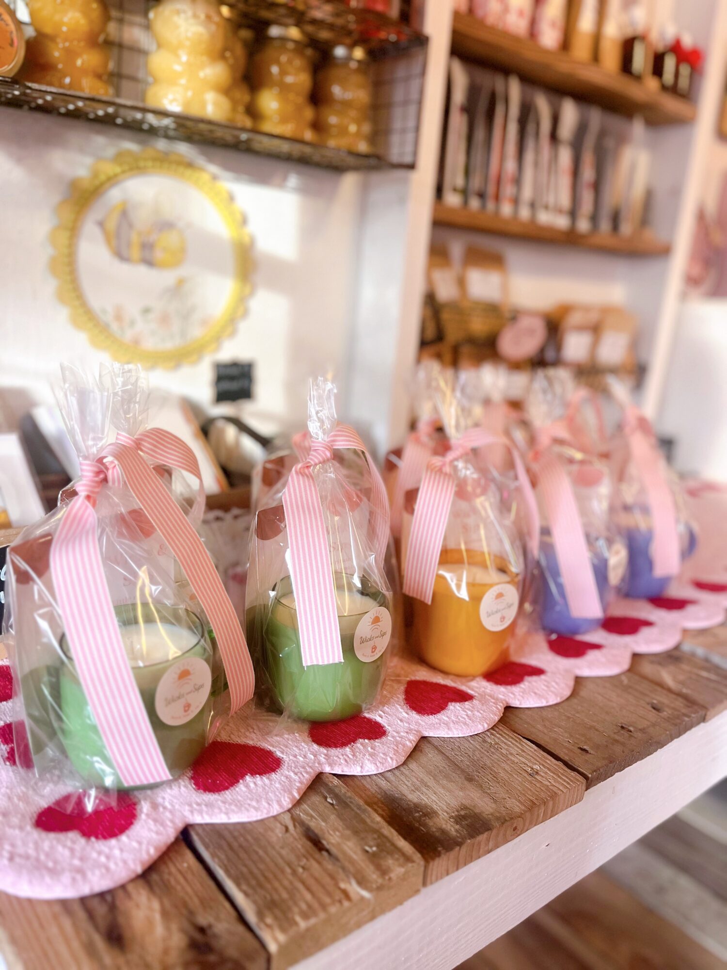 Colorful wrapped candies in clear bags with pink ribbons on a wooden table, decorated with a pink and white cloth, in a shop.
