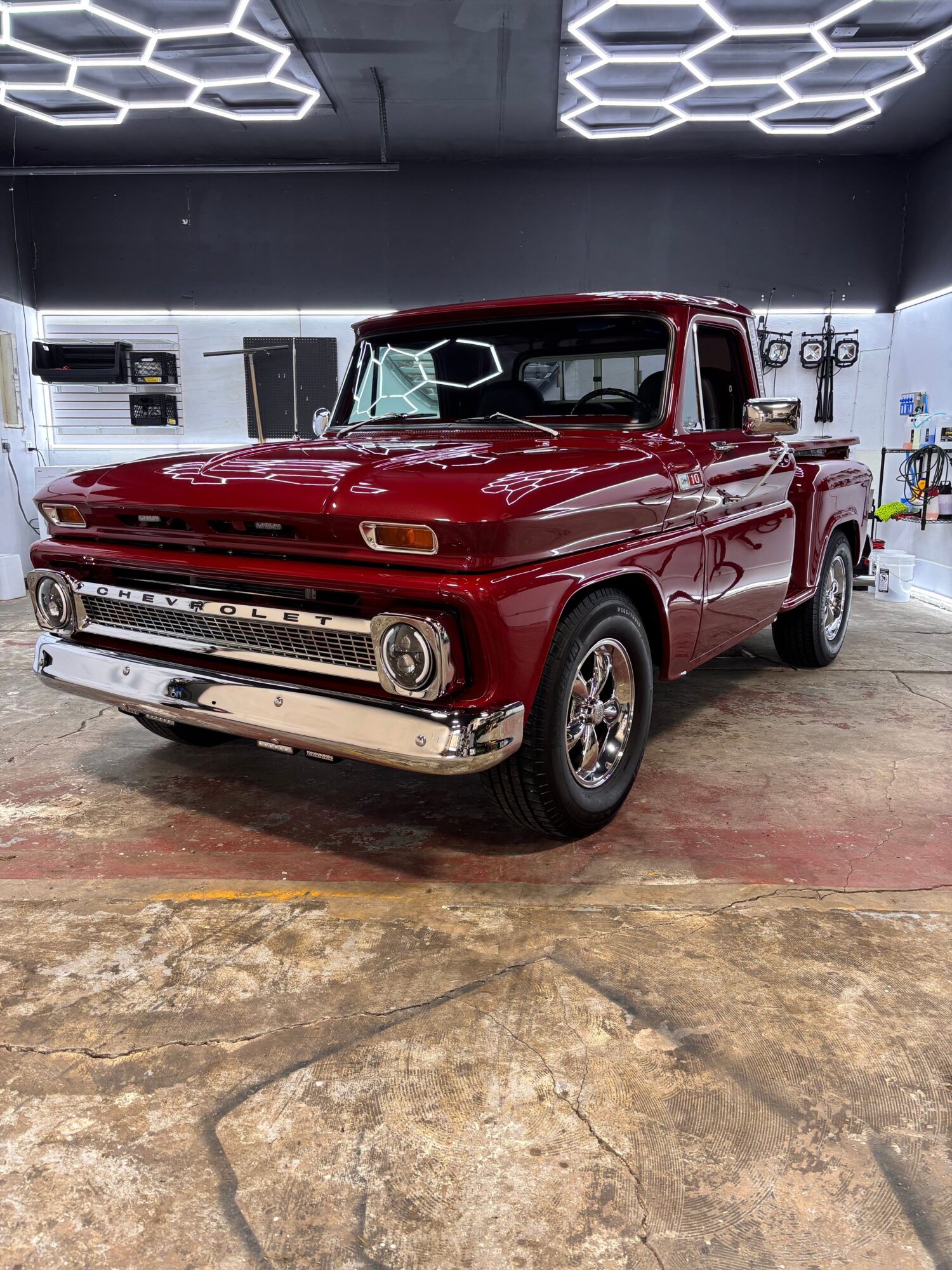 Red vintage pickup truck parked indoors with a concrete floor and modern lighting, viewed from the side.