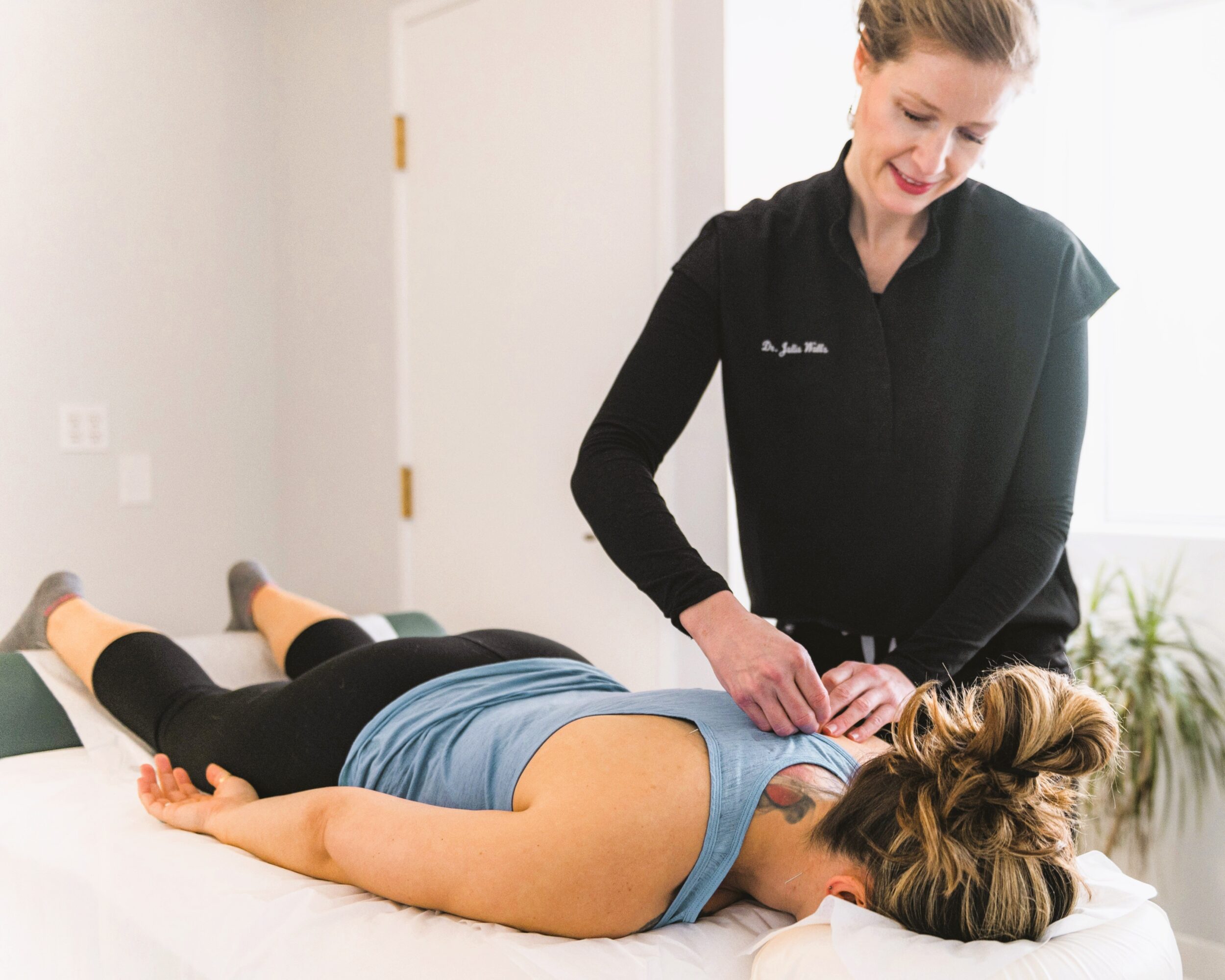 A woman receives a chiropractic adjustment from a healthcare professional lying face down on a treatment table.