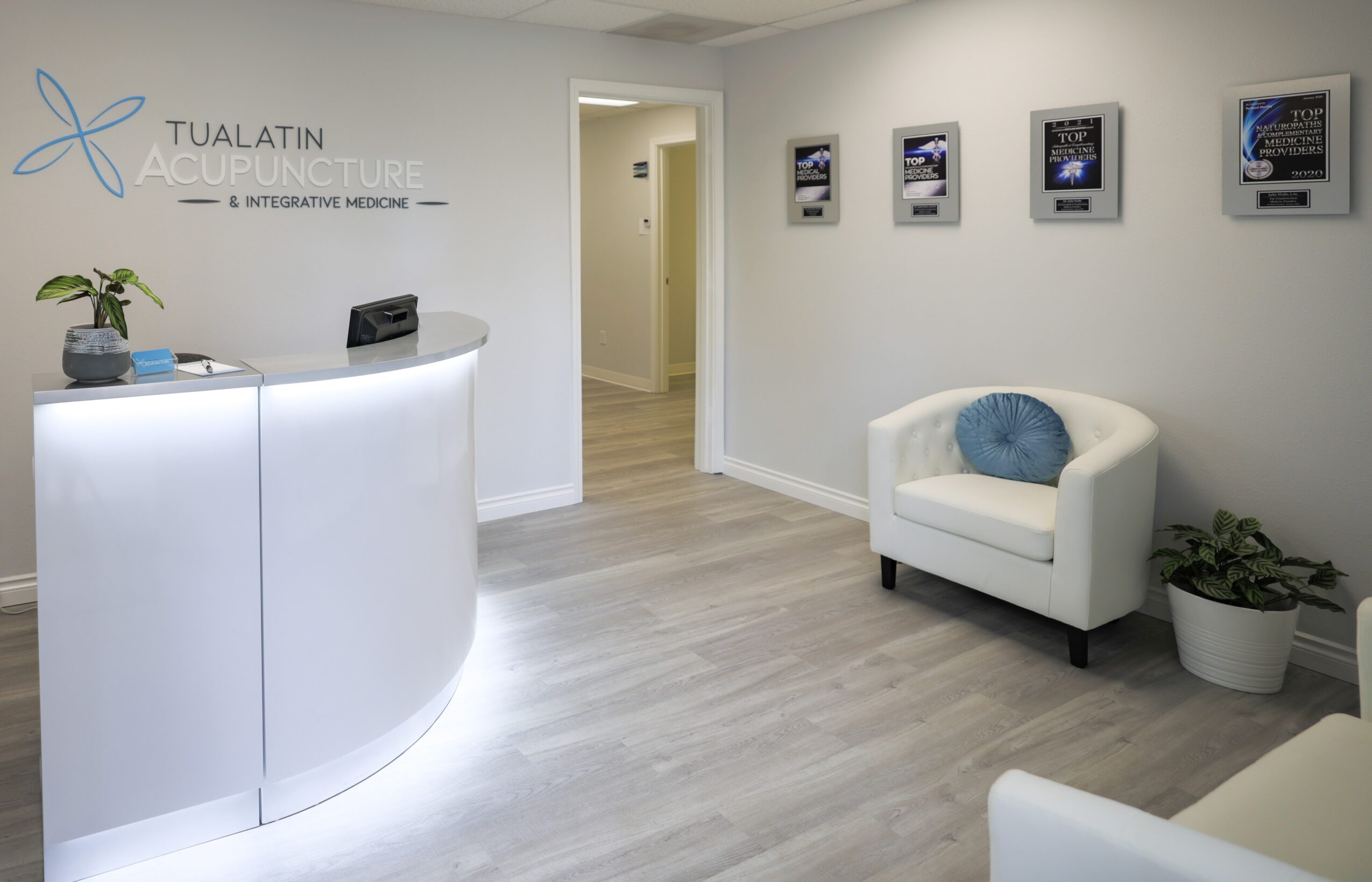 Reception area with a curved white desk, a white armchair with a blue pillow, and framed screens on the wall.