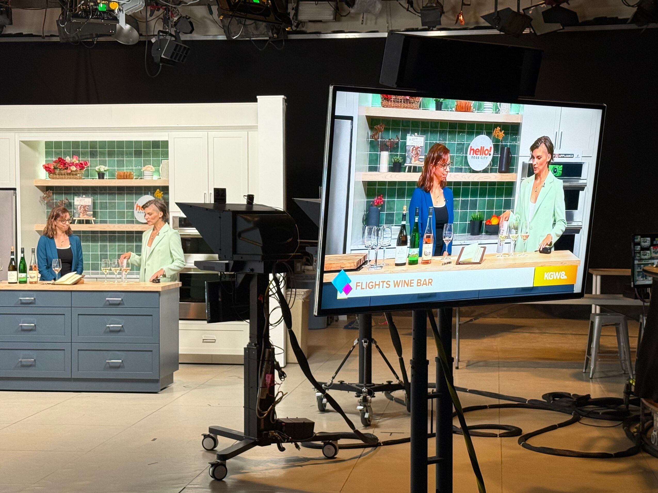 Two women and a girl in a kitchen set, with shelves and a counter, on a TV screen and in the studio.