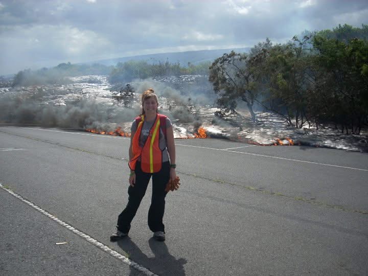 Person standing on road near a wildfire with smoke and flames in the background.
