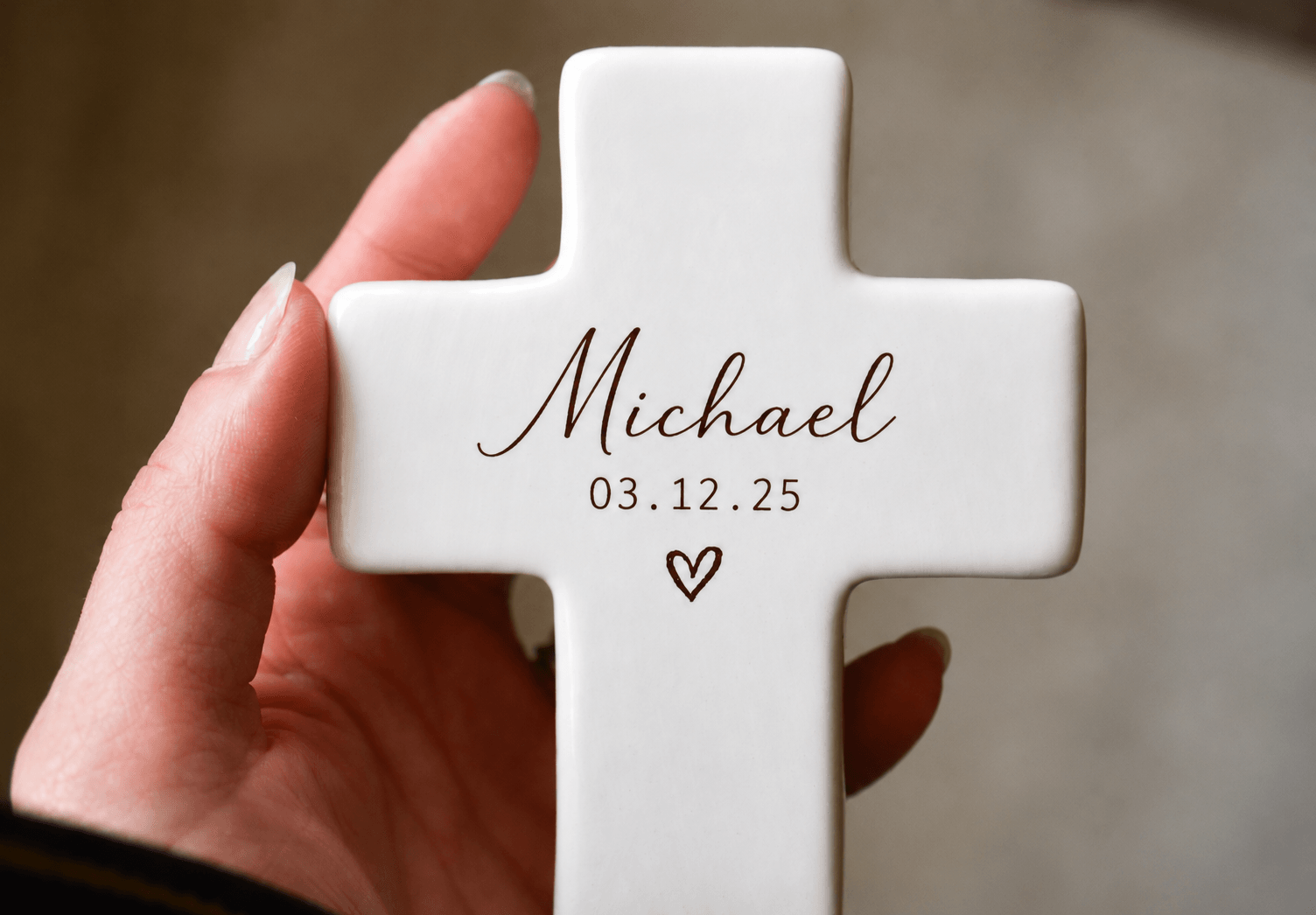 Hand holding a white cross-shaped object with the name Michael, date, and a heart symbol.