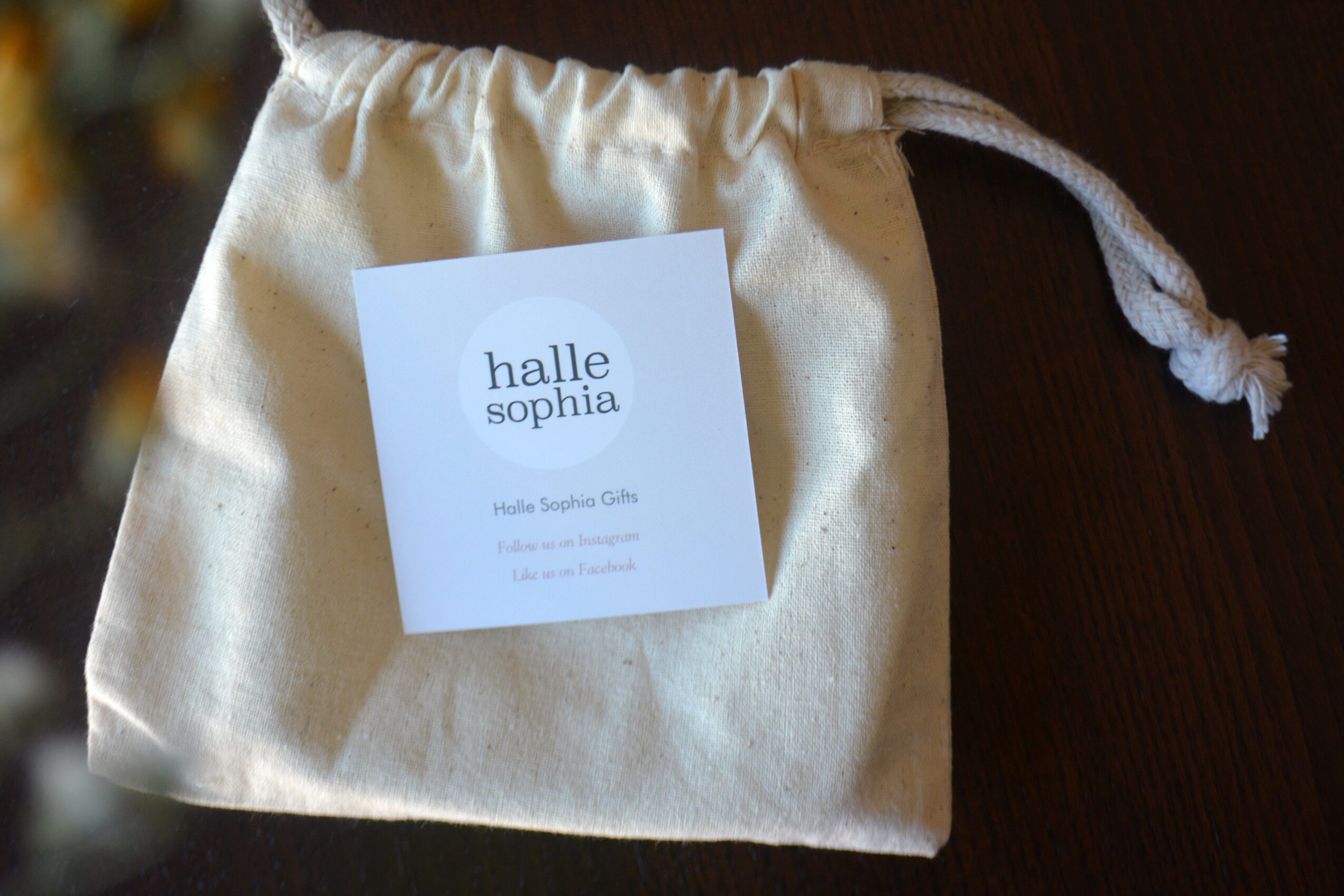 Cream-colored drawstring bag with a white card inside, placed on a dark surface.
