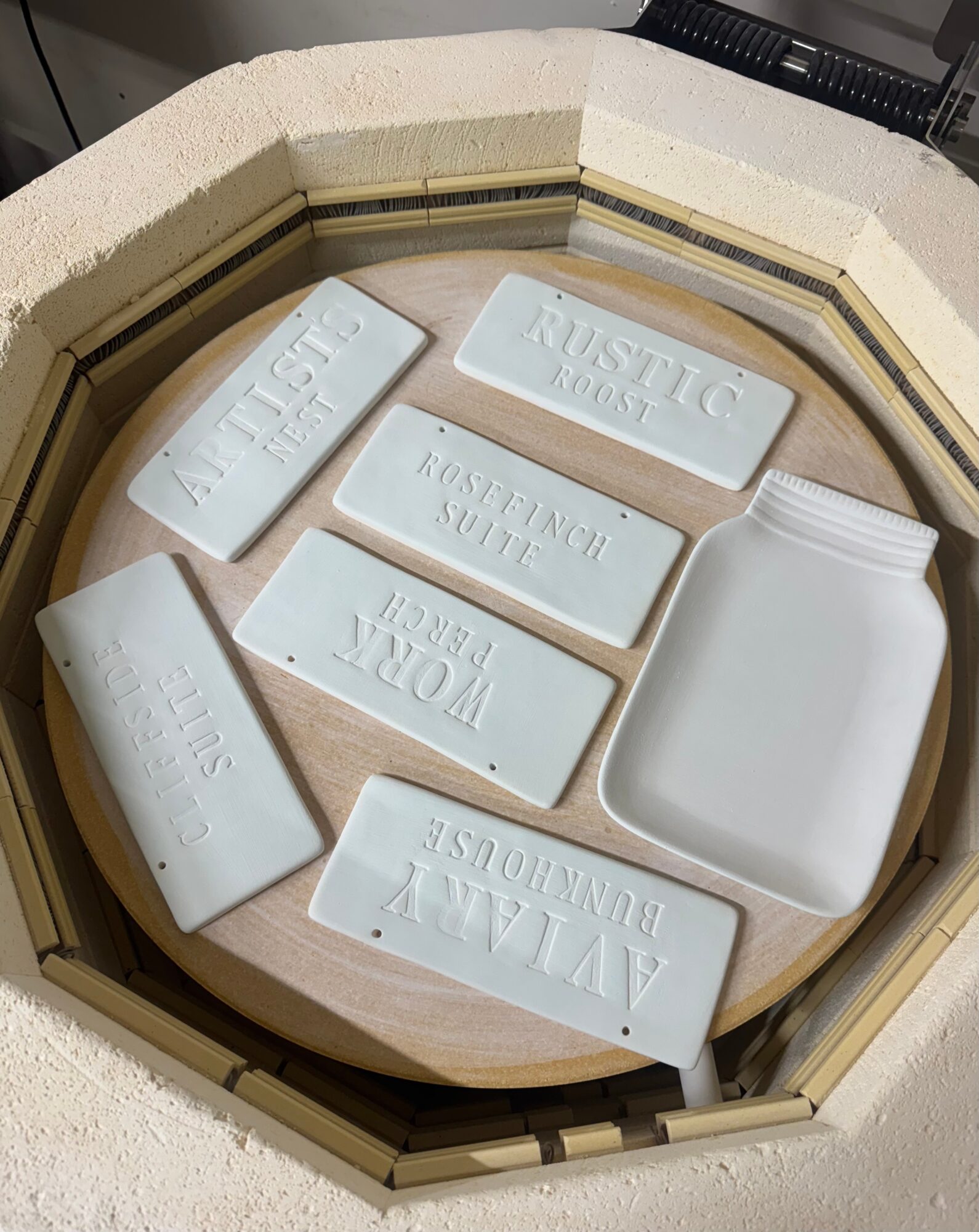 Clay molds with various engraved words and a white container inside a kiln, viewed from above.