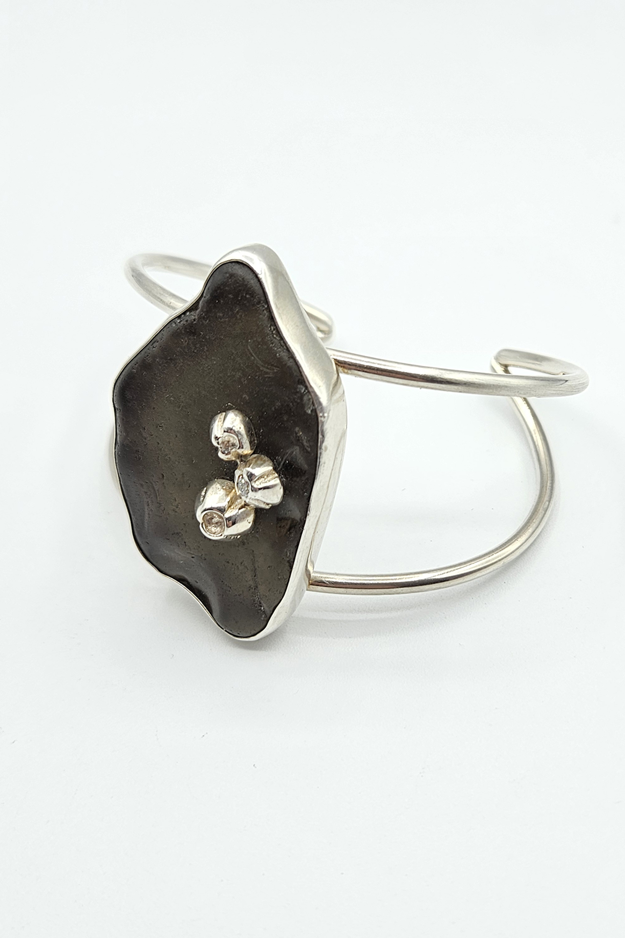 Silver bracelet with a black irregular-shaped stone and small decorative elements, on a white background.