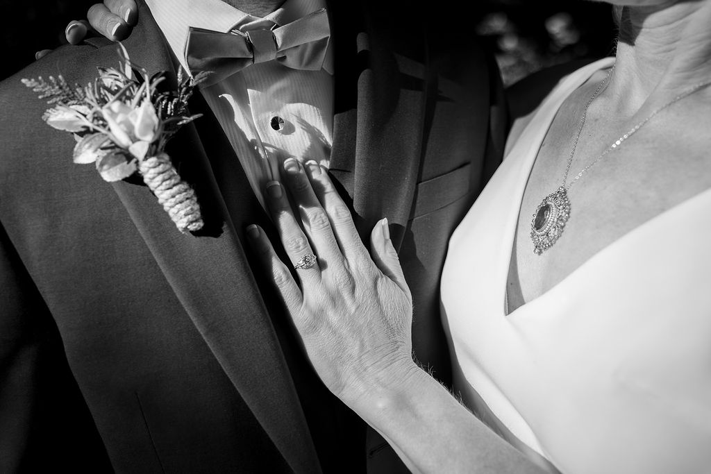 Close-up of a woman touching a man's chest, both dressed in formal attire, with a corsage and necklace visible.
