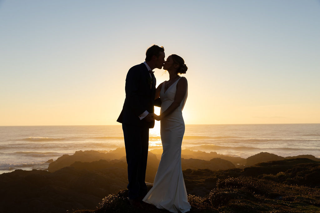 Silhouette of a couple holding hands and touching foreheads on a beach at sunset.