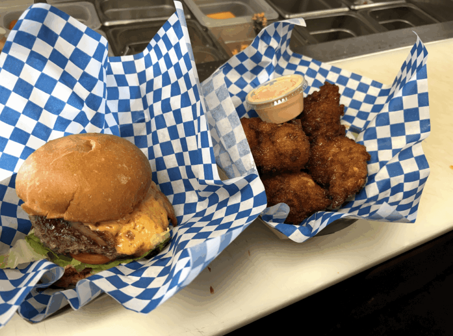 Burger with bun, lettuce, and patty next to fried chicken pieces with dipping sauce, on blue checkered paper.