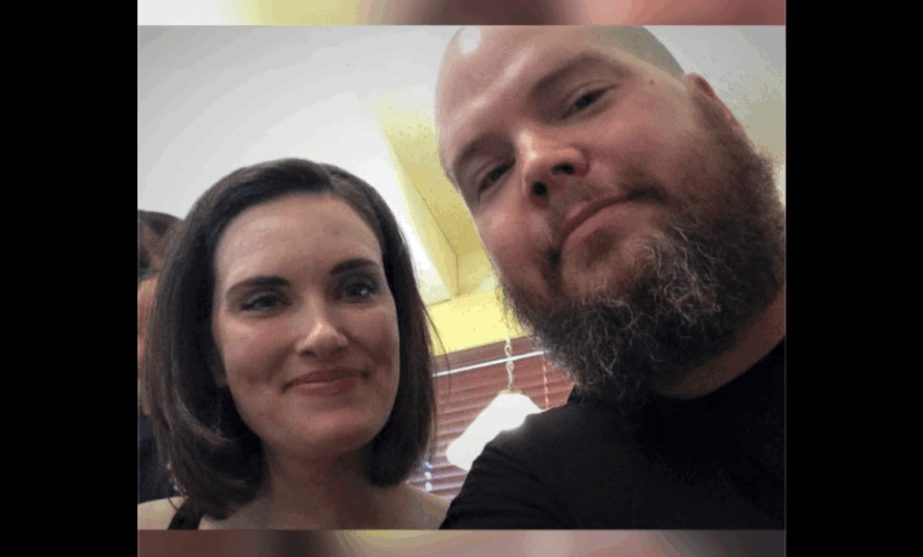 Two people taking a selfie, one woman and one man, with blurred background.