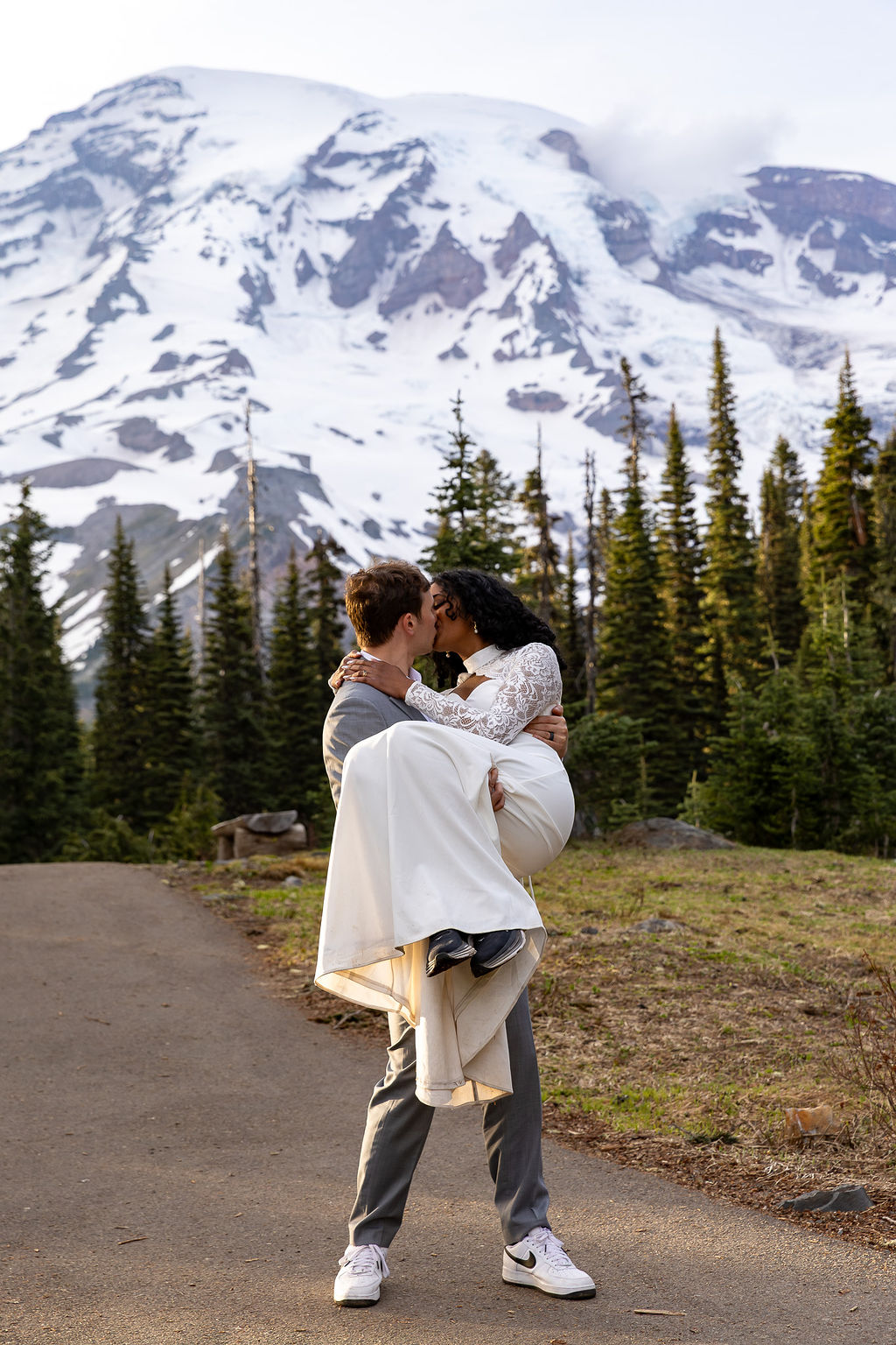 Person carrying another person outdoors with snow-capped mountain and trees in background