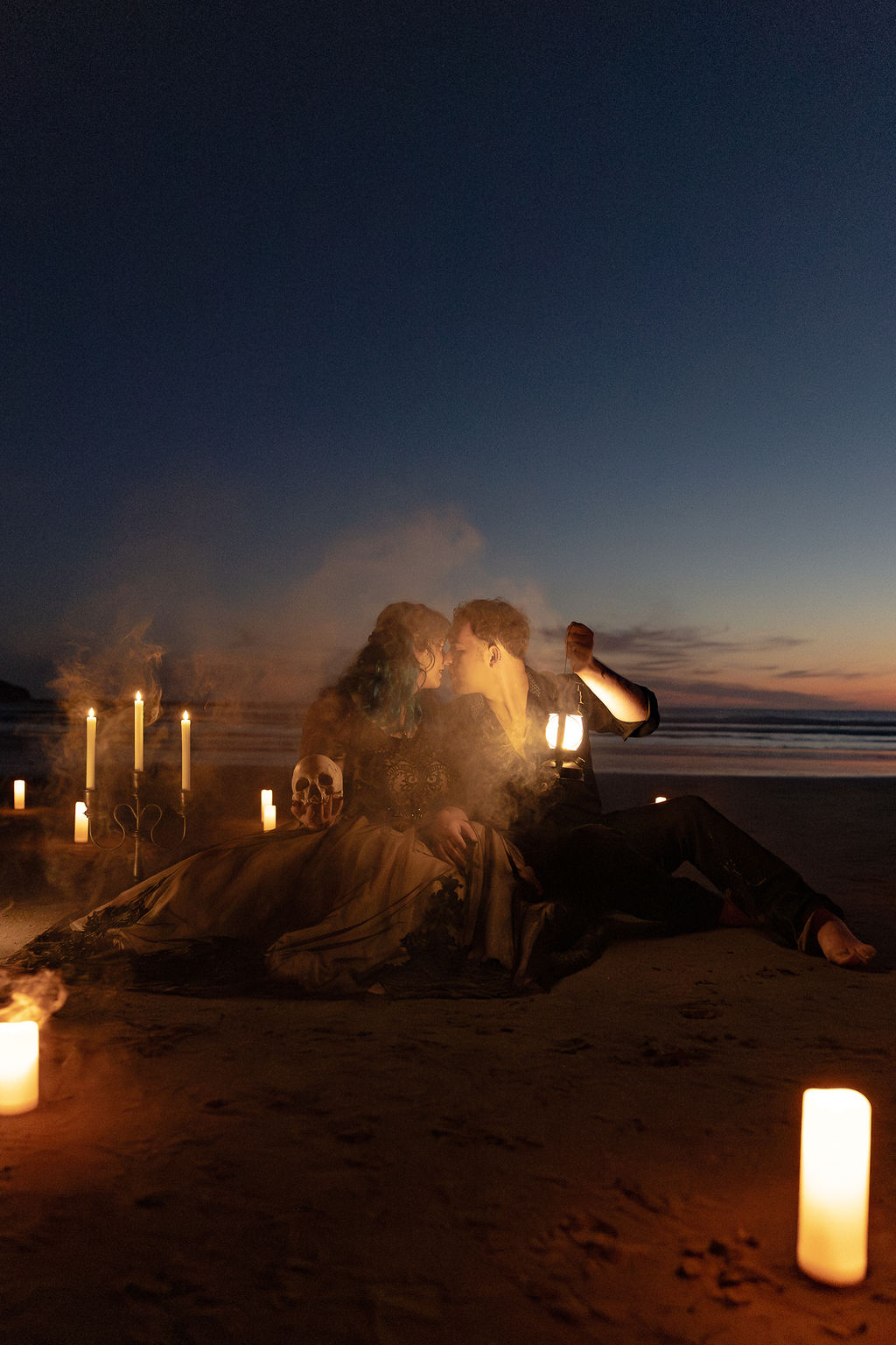 Person sitting on the beach at night with candles around, looking at the ocean horizon, sky darkening.