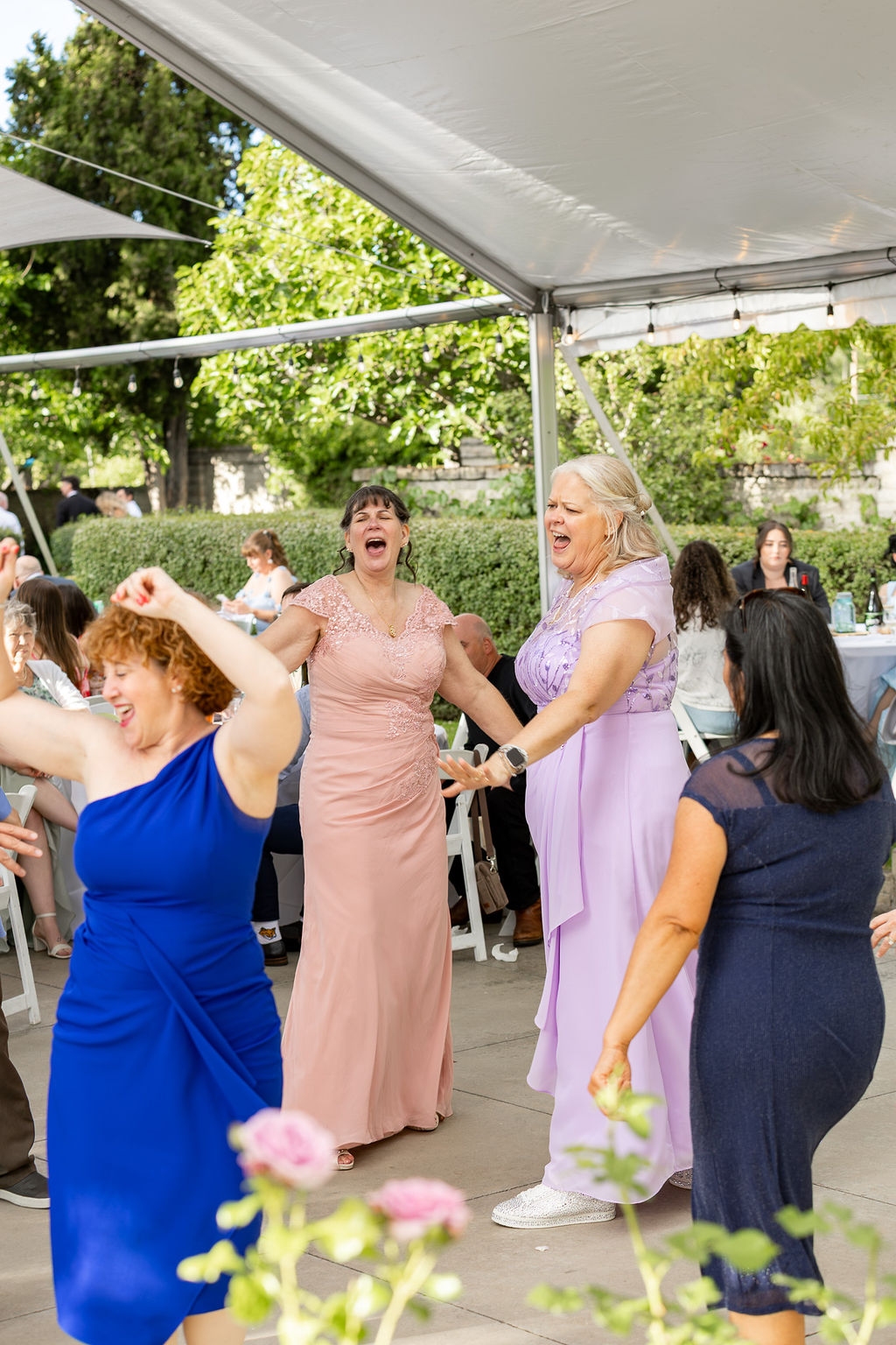 People dancing and celebrating outdoors under a tent, with trees and sunlight in the background.