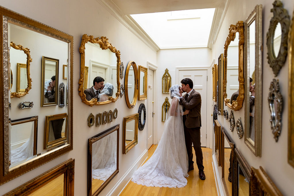 A bride and groom dance in a hallway with ornate gold-framed mirrors on the walls.