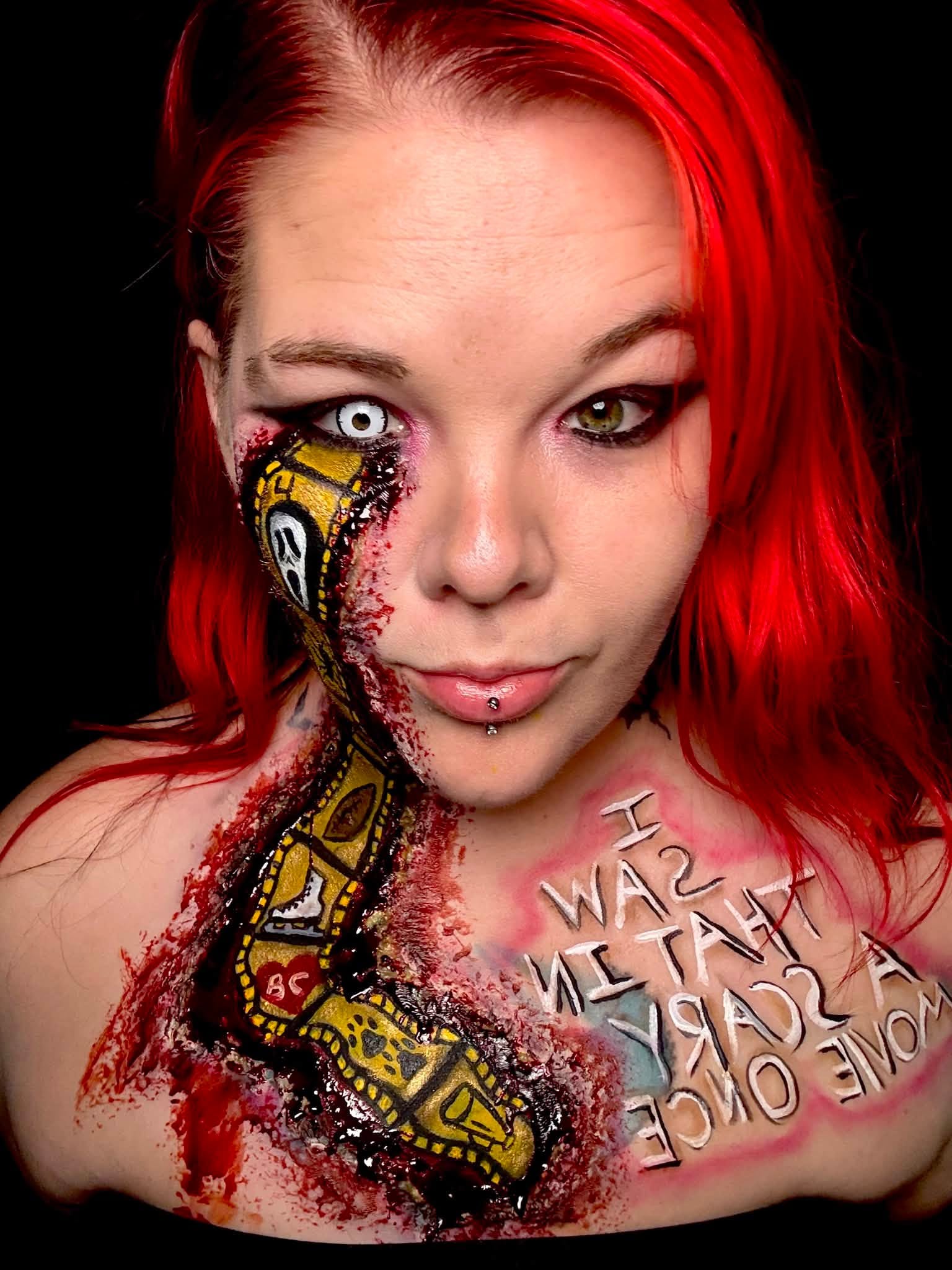 Woman with red hair and face paint, a snake tattoo on her shoulder, and text on her chest.