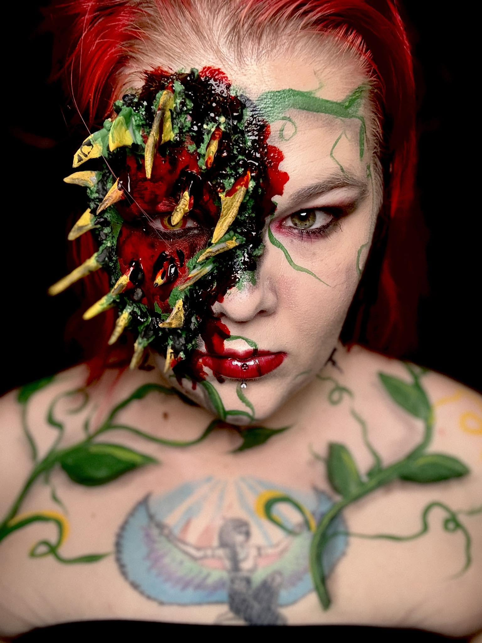 Person with half face painted and decorated with a large, colorful, monster-like mask covering one eye, red hair, and tattoos.