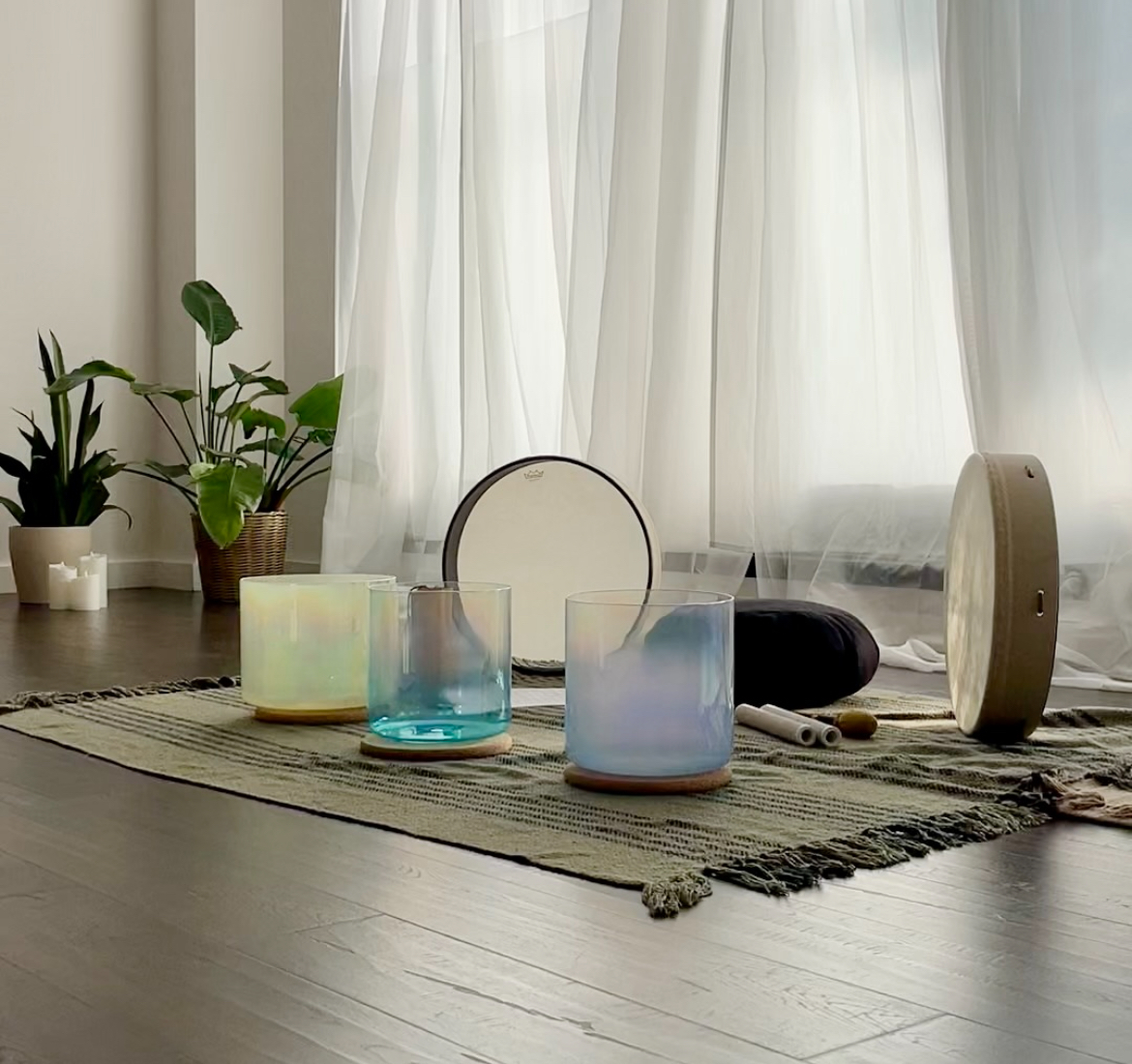 Glassware and musical instruments on a striped rug in front of a window with white curtains, with potted plants nearby.