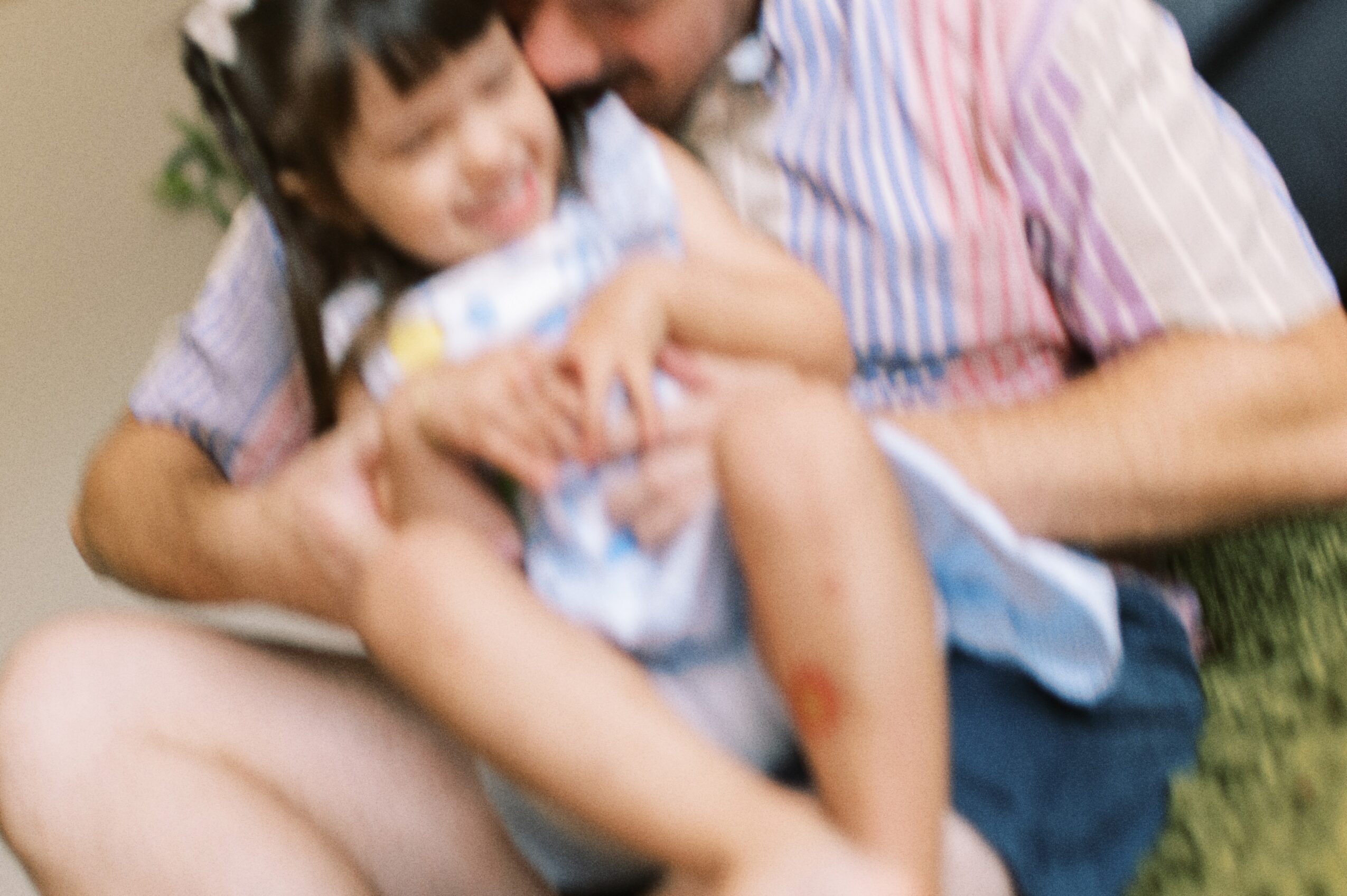 Two people sitting closely, one holding a young girl, both smiling and embracing outdoors.