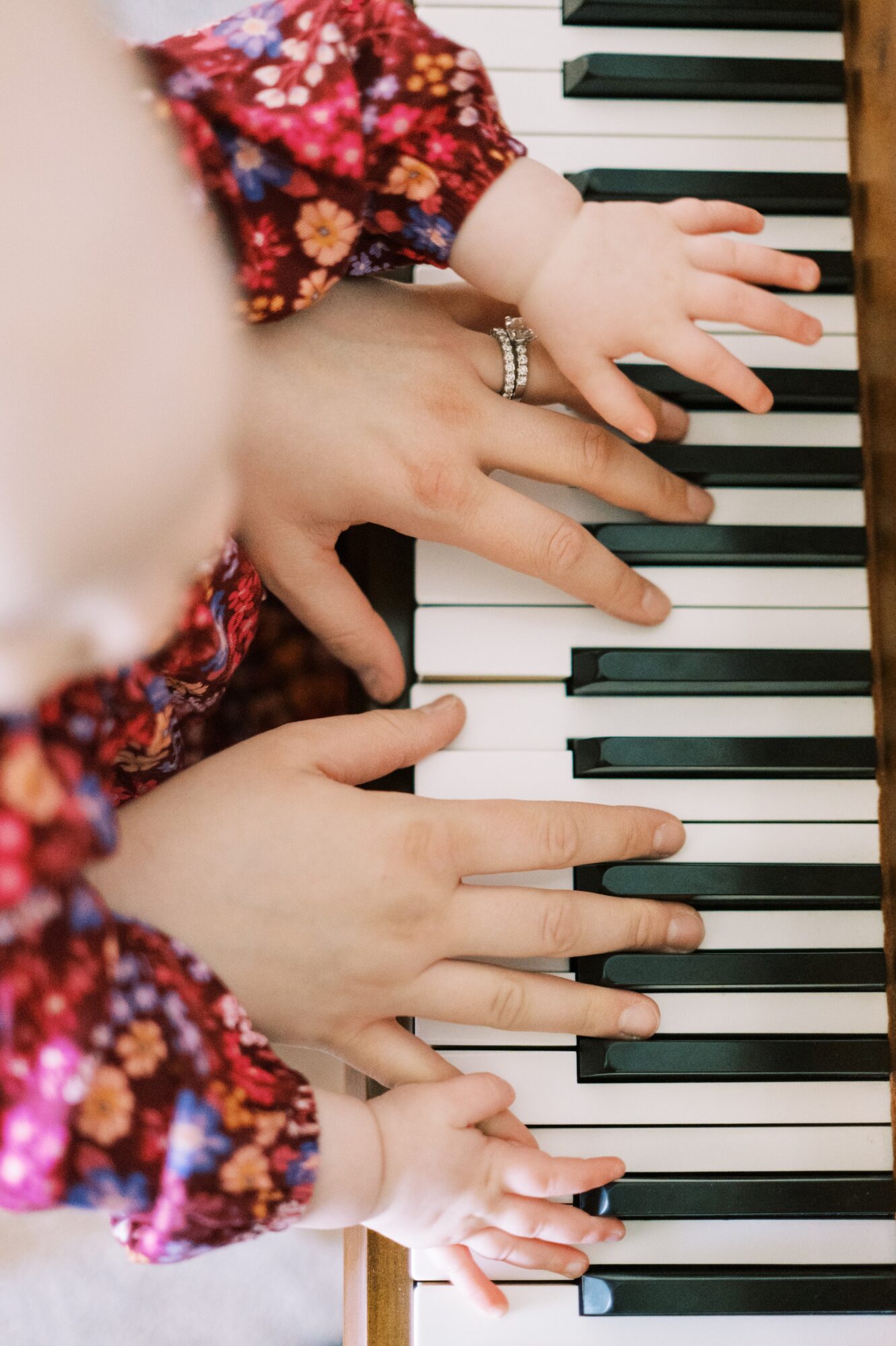 Two children and an adult's hands playing piano keys, wearing colorful clothing, with a focus on hands and keyboard.