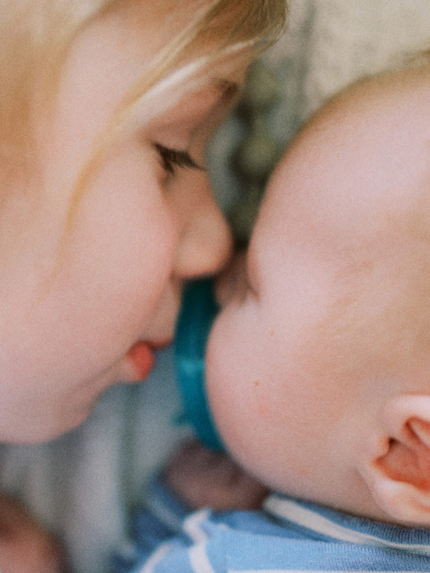 Close-up of a woman and a baby touching noses, both with eyes closed, in a tender moment.