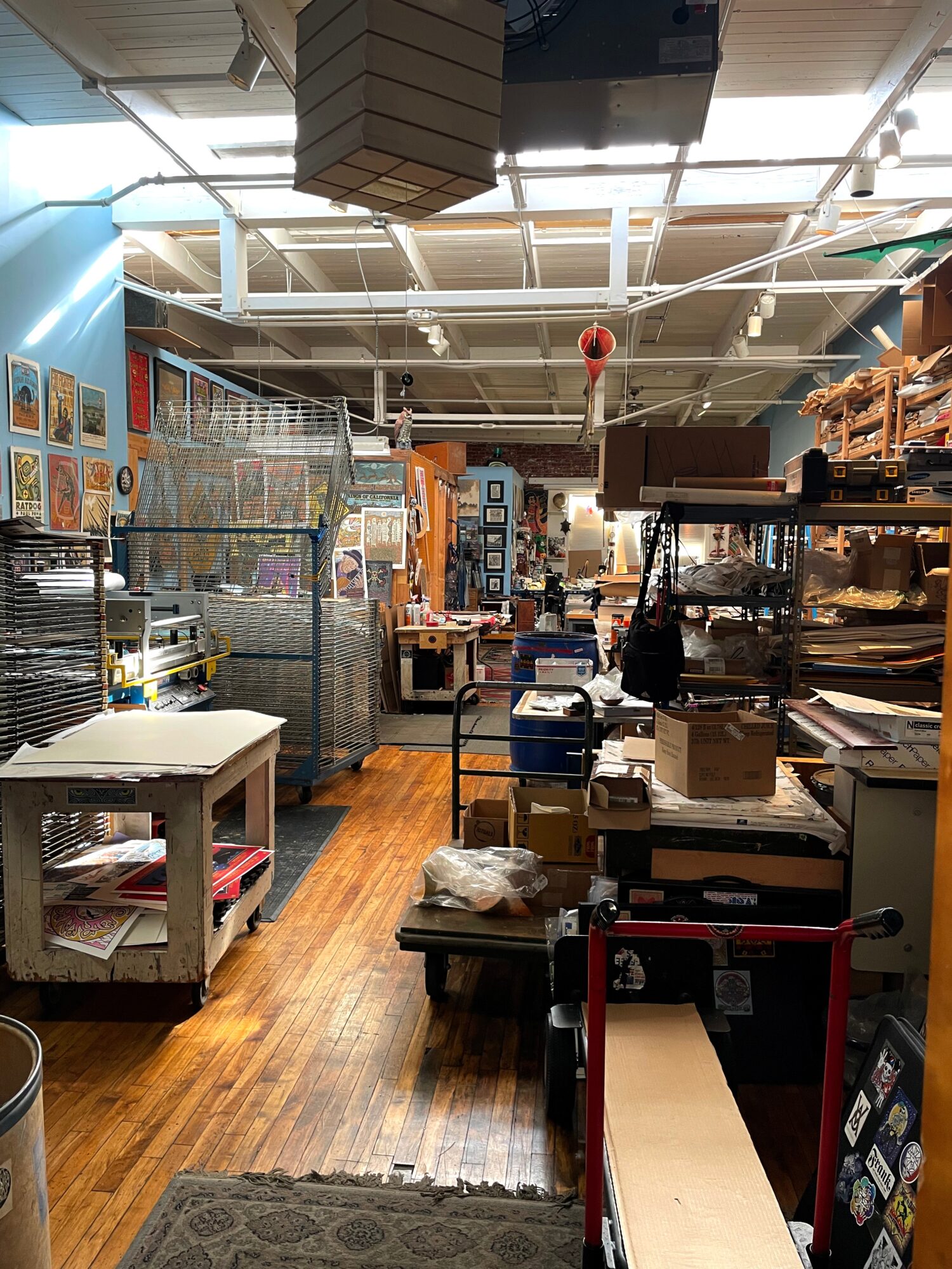View of a store aisle with shelves filled with various items, a table on the left, and a wooden floor.