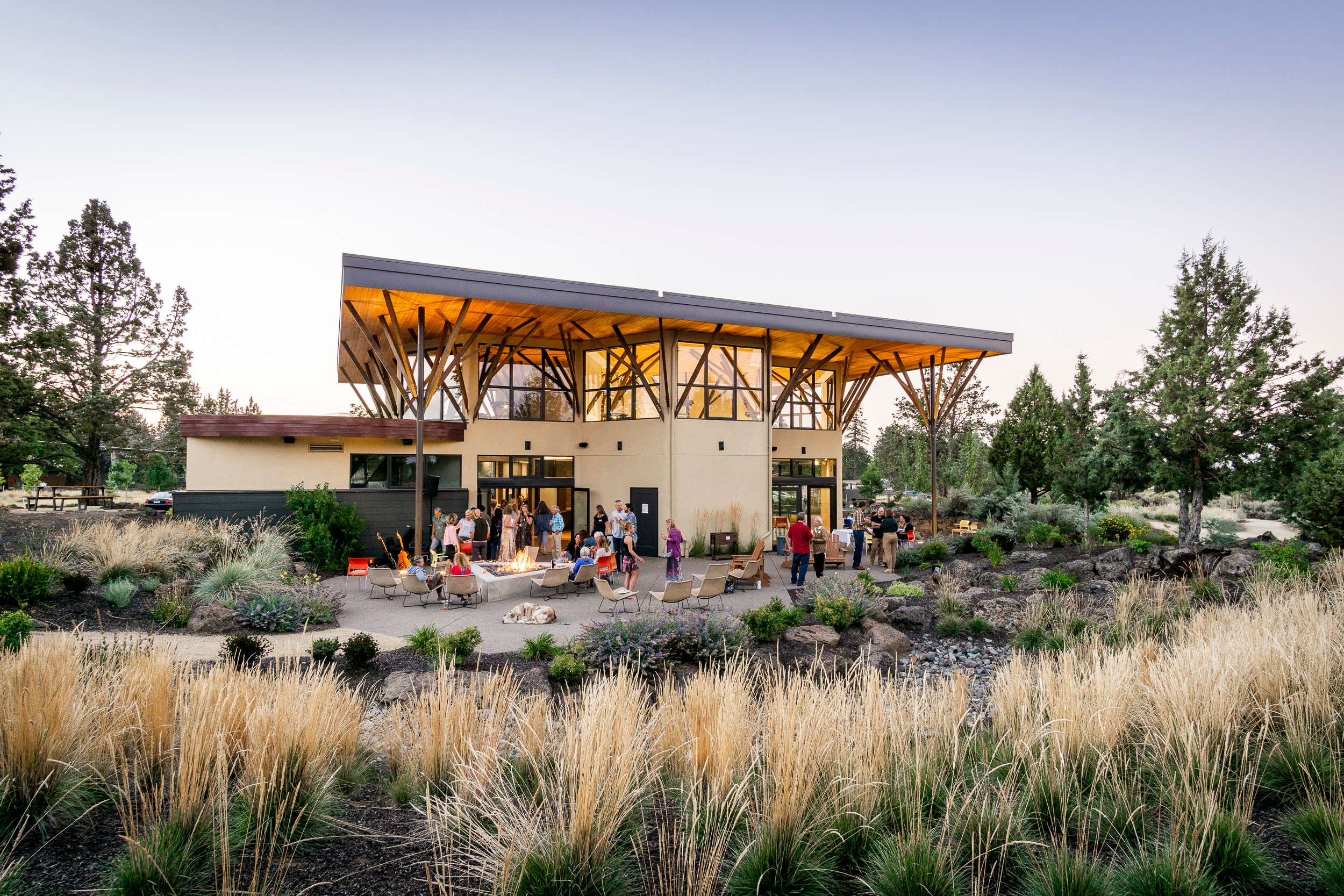 Modern building with a sloped roof, surrounded by trees and people, in a landscaped outdoor area.
