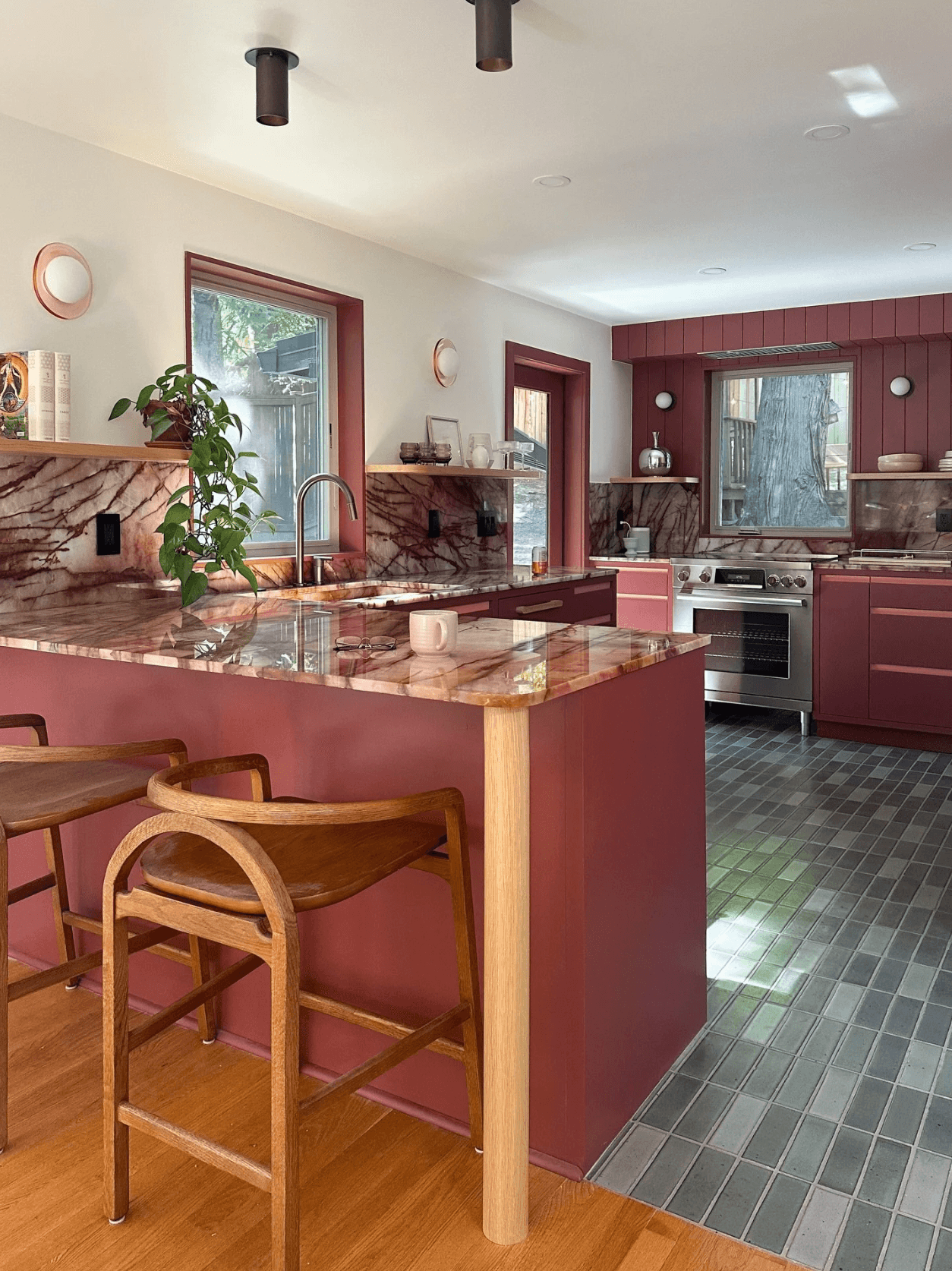 Kitchen with pink cabinets, marble countertop, and two wooden chairs at the counter, with windows and a tiled floor.
