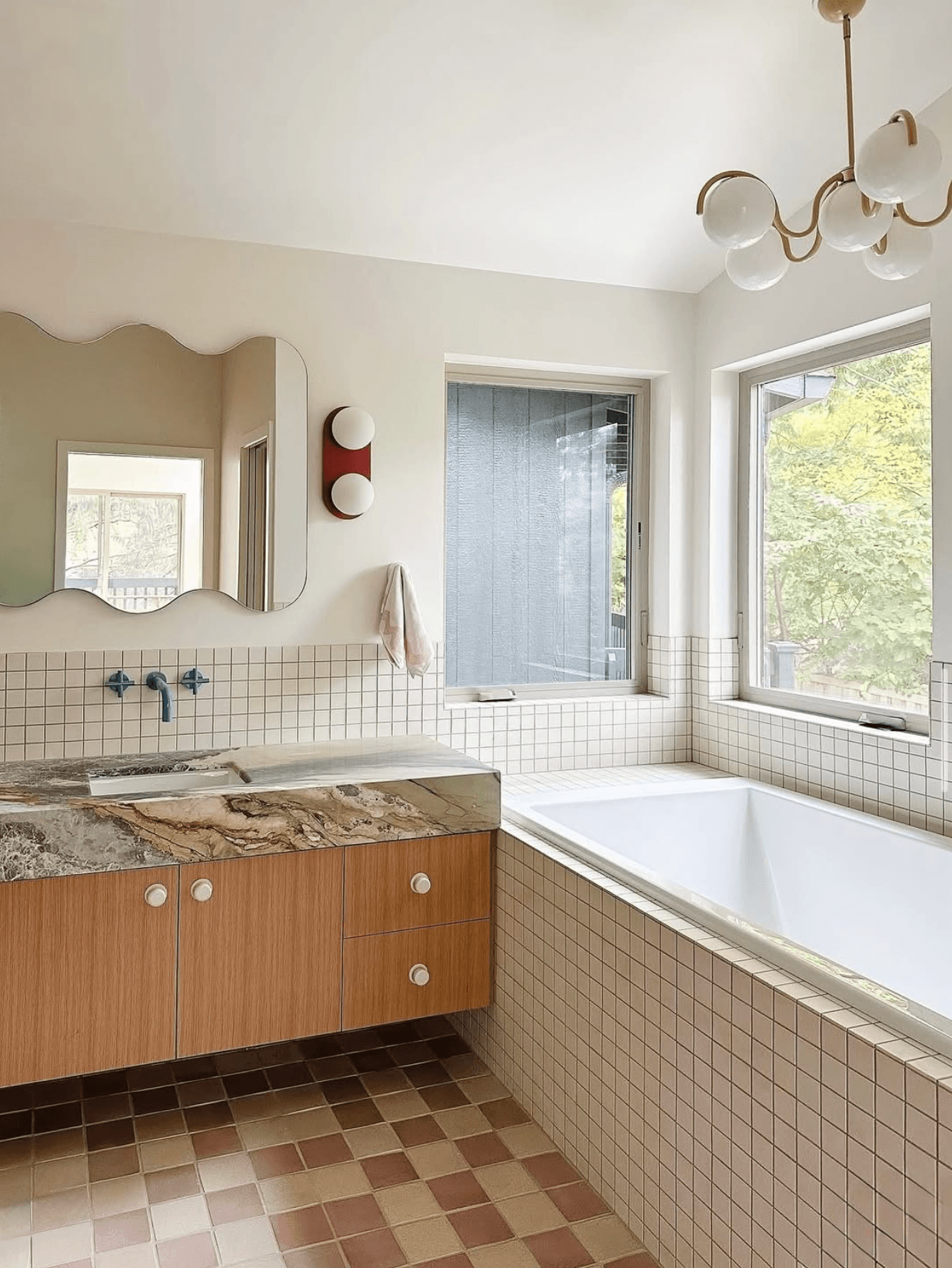 Bathroom with a bathtub, window, mirror, and wooden cabinet, featuring tiled walls and a patterned floor.