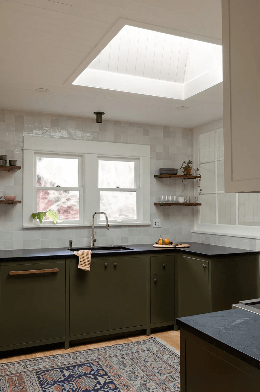 Kitchen with green cabinets, white window, open shelves, and a skylight ceiling, with a patterned rug on the floor.