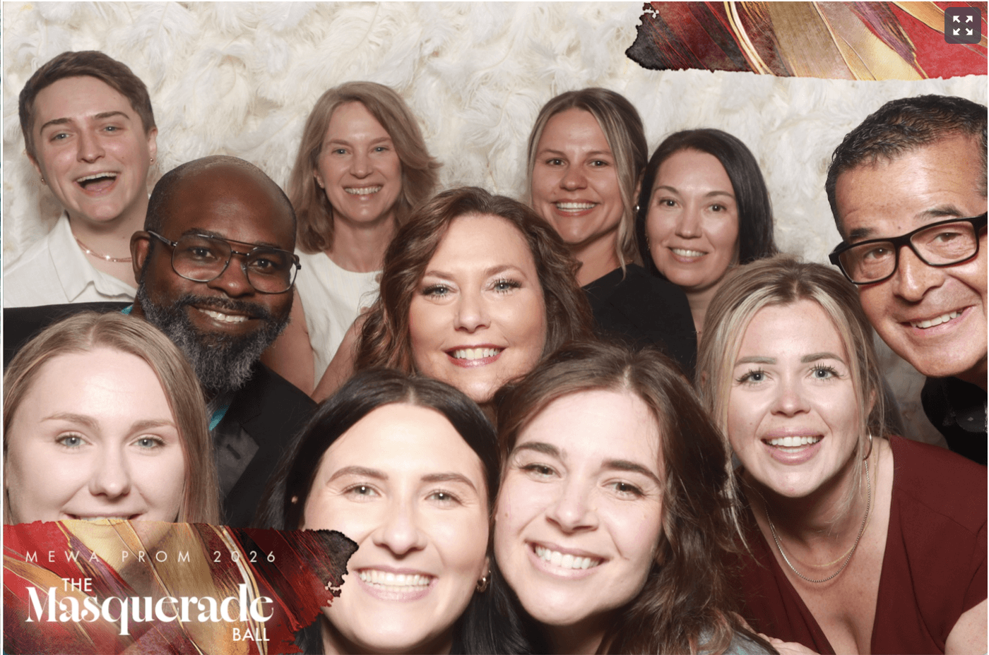 Group of ten smiling people taking a selfie together at an event, with a textured background.