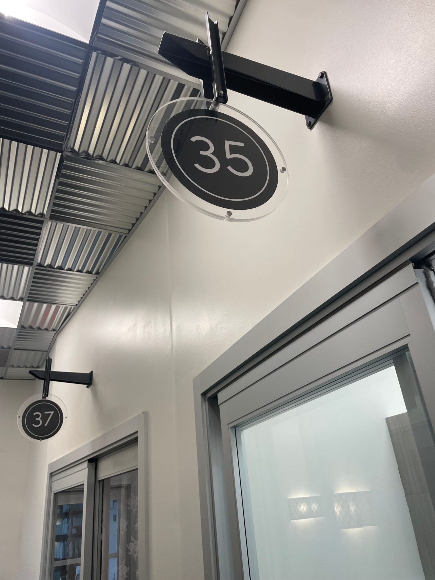 Ceiling with two circular signs displaying numbers 35 and 37, and windows with blinds, in a modern interior.