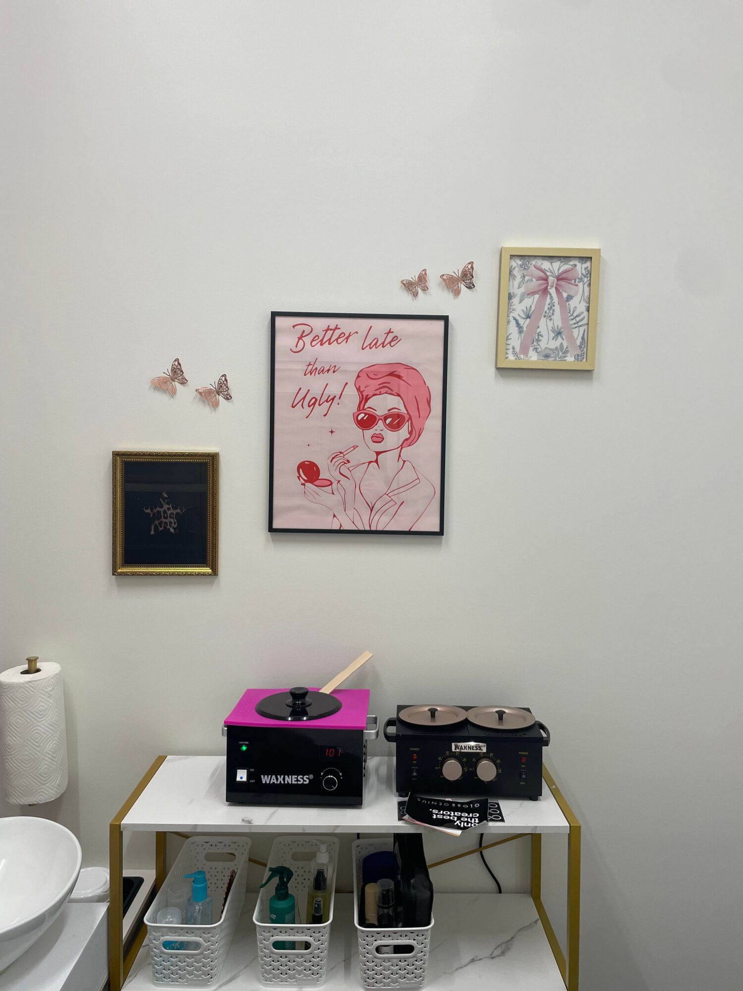 Wall with framed artwork and butterfly decorations, with a shelf holding electronic devices and a white container below.