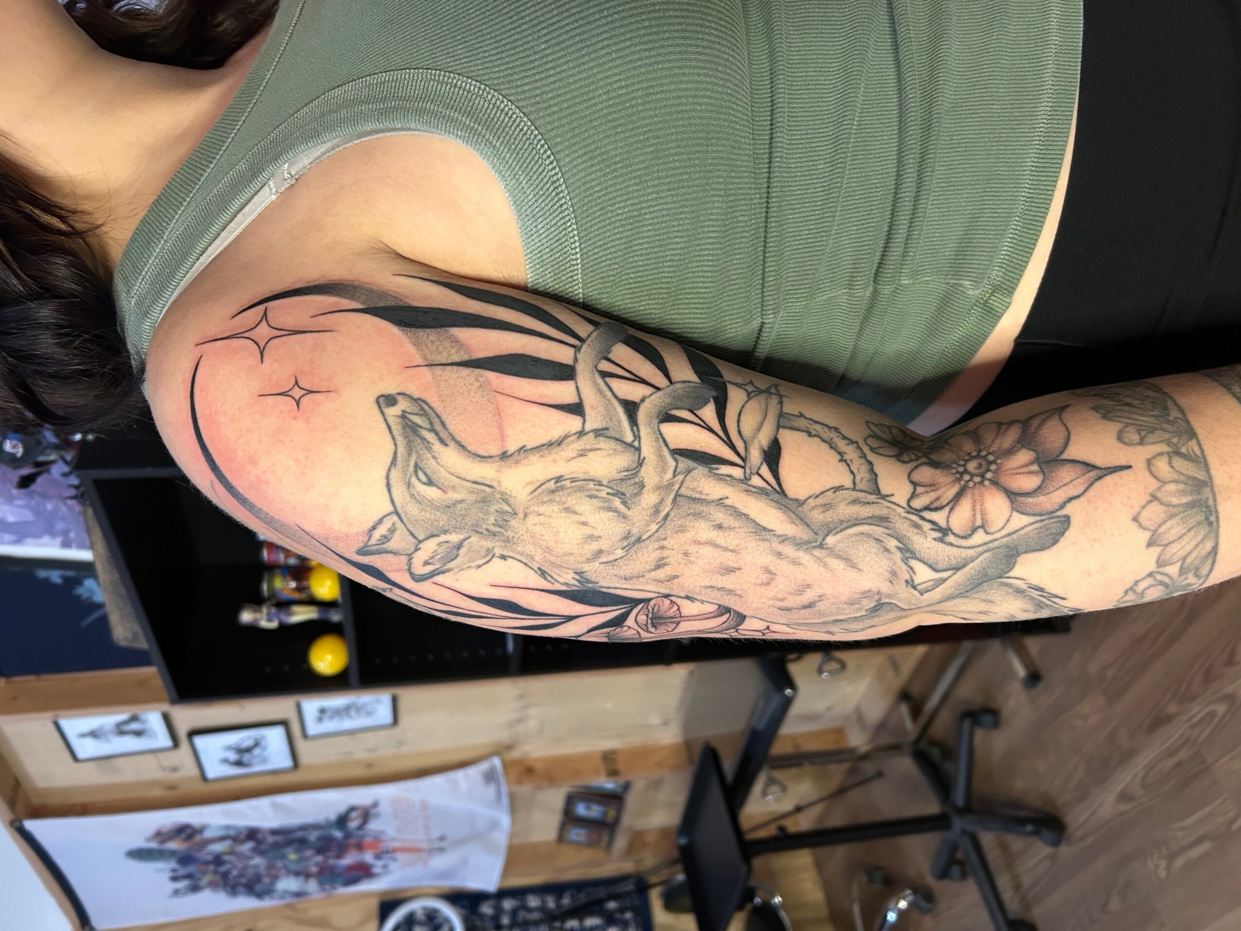 Person with a large tattoo of a wolf on their arm, wearing a green tank top, in a room with pictures and furniture.