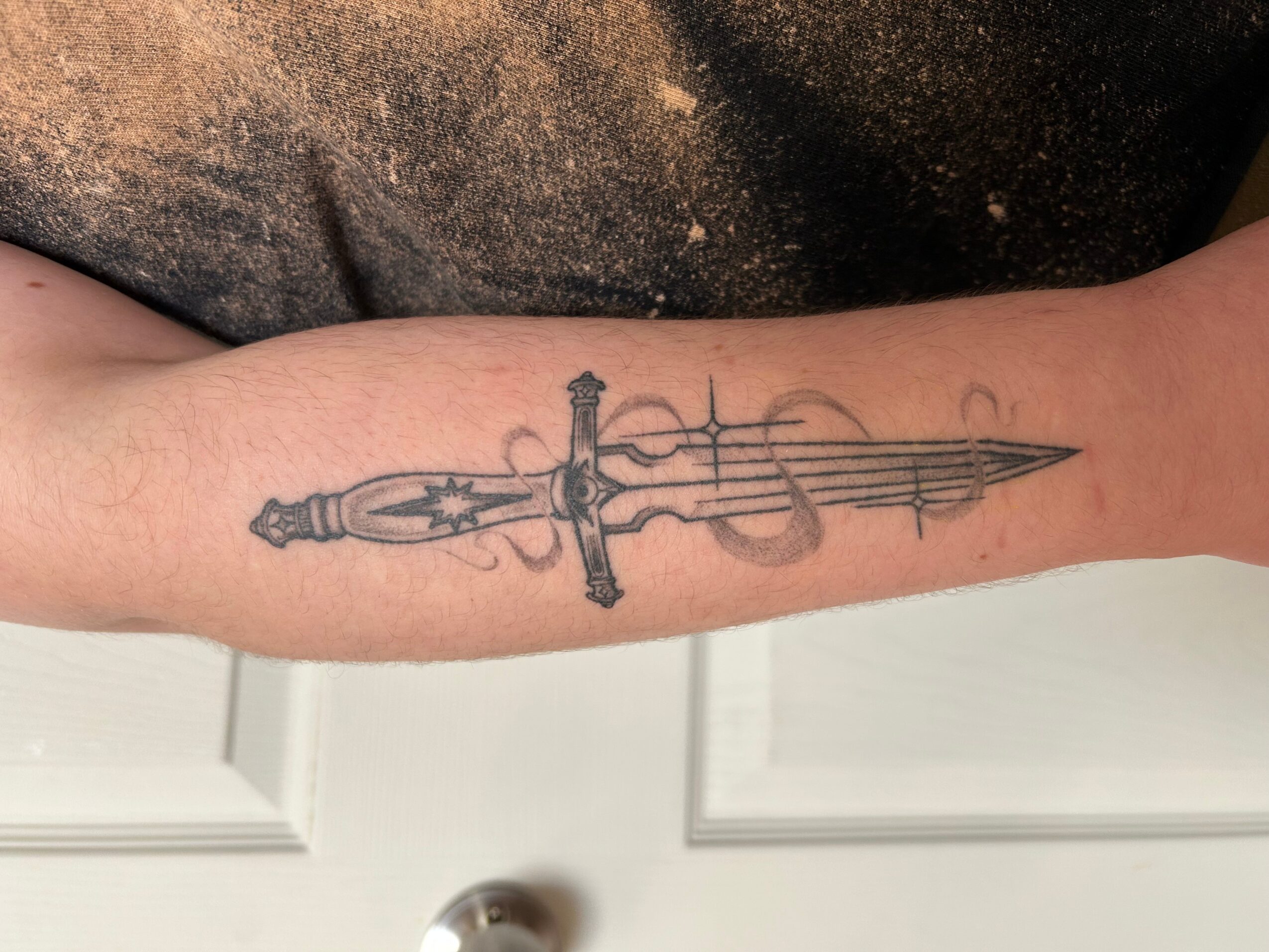 Tattoo of a sword with a detailed hilt and a long, pointed blade on a person's forearm.