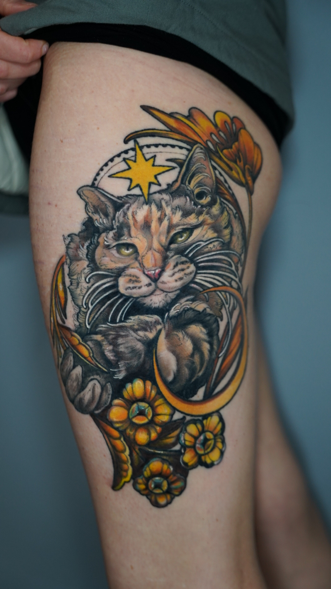 Colorful tiger tattoo with flowers, stars, and feathers on person's thigh.