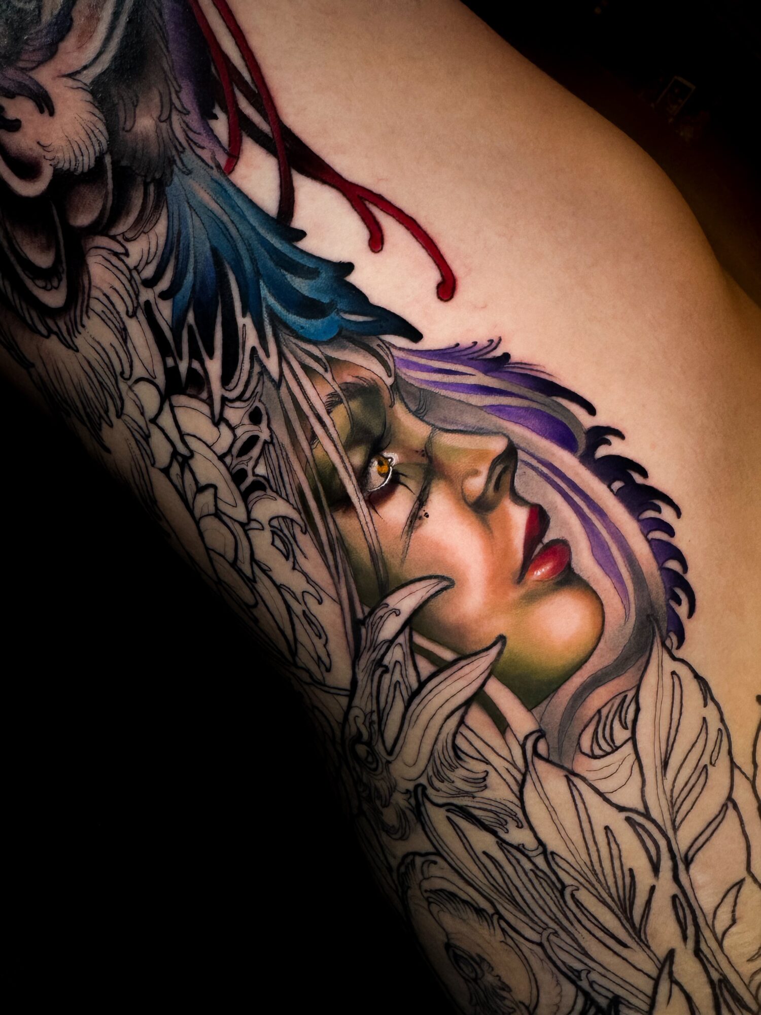 Tattoo of a woman's face with colorful hair and feathers on a person's shoulder, detailed and vibrant.