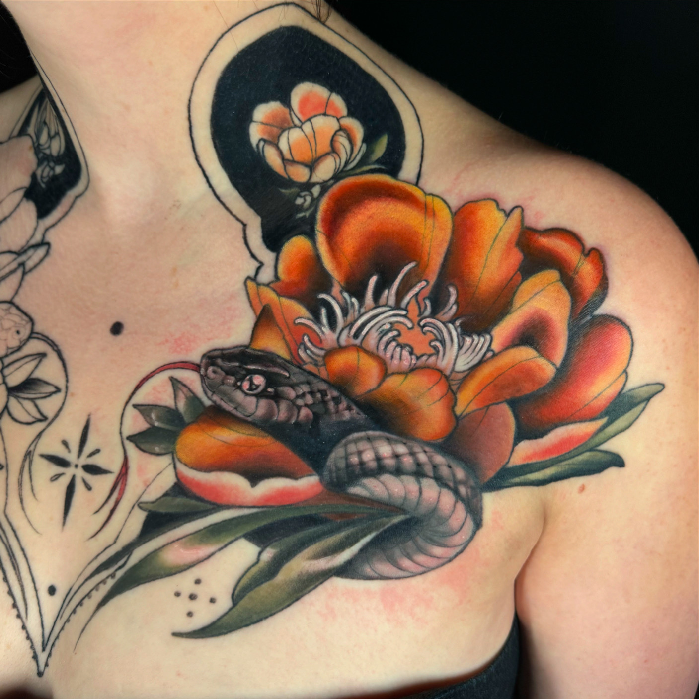 Tattoo of a snake coiled around a large orange flower with green leaves, and a circular design above. Bright colors and detailed shading.