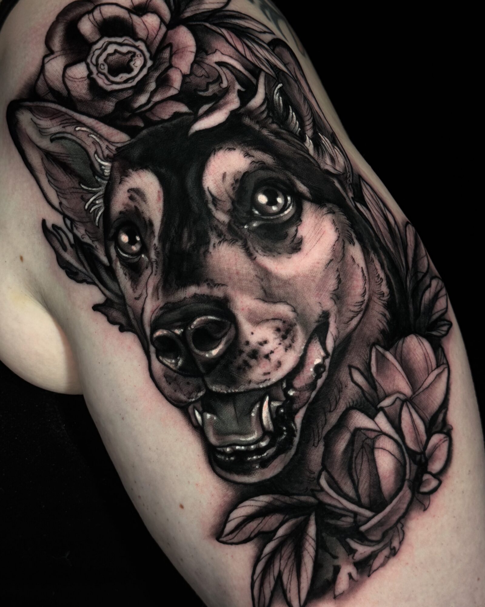 Tattoo of a dog's face surrounded by flowers on person's shoulder, detailed and realistic style.