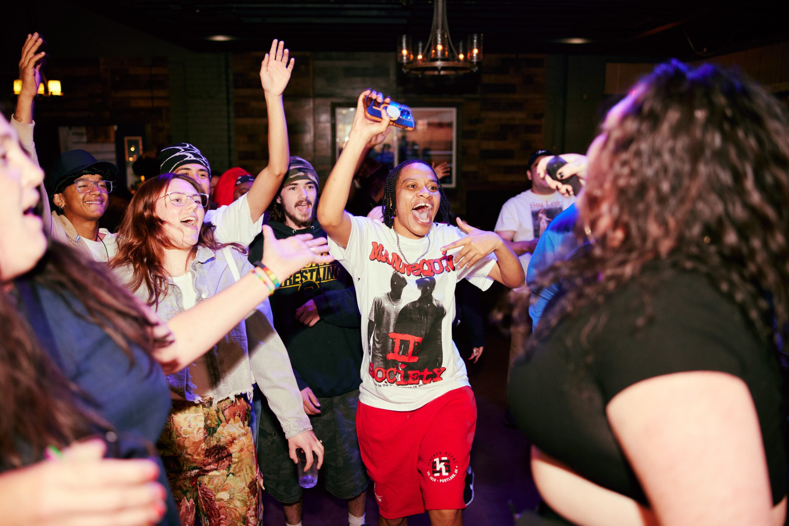 Group of people dancing and raising hands in a lively indoor setting, smiling and enjoying themselves.