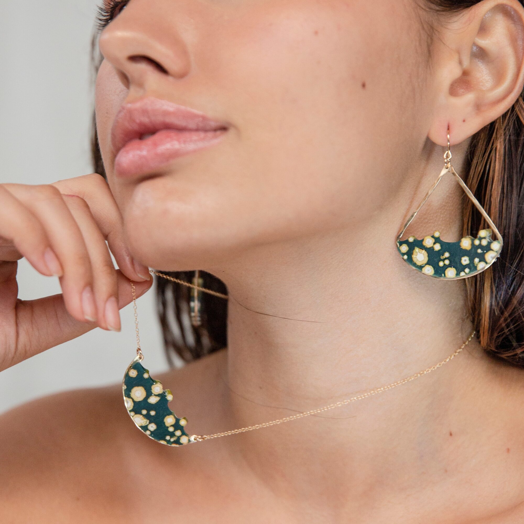 Close-up of a woman wearing a matching necklace and earring set with green and gold polka dot design.