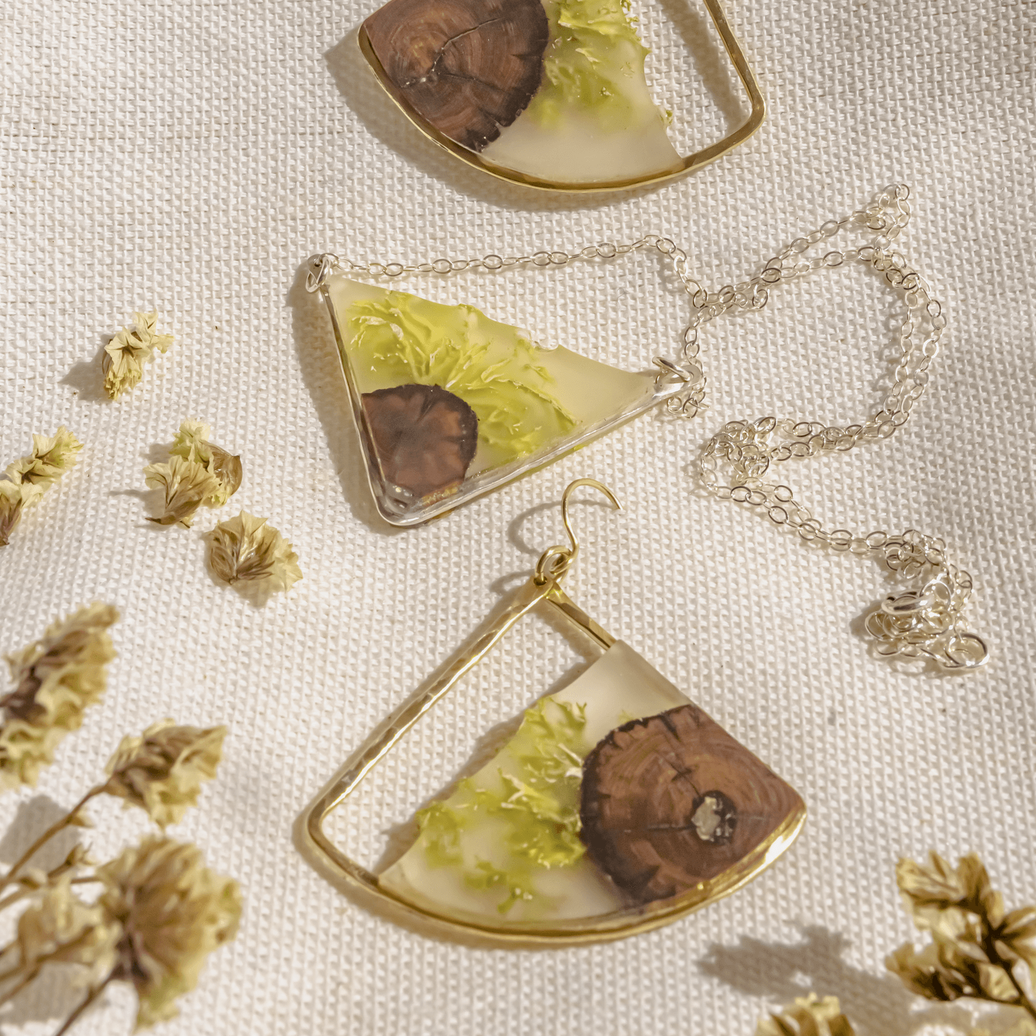 Jewelry pieces with glass and leaf designs, surrounded by small dried flowers on a textured surface.